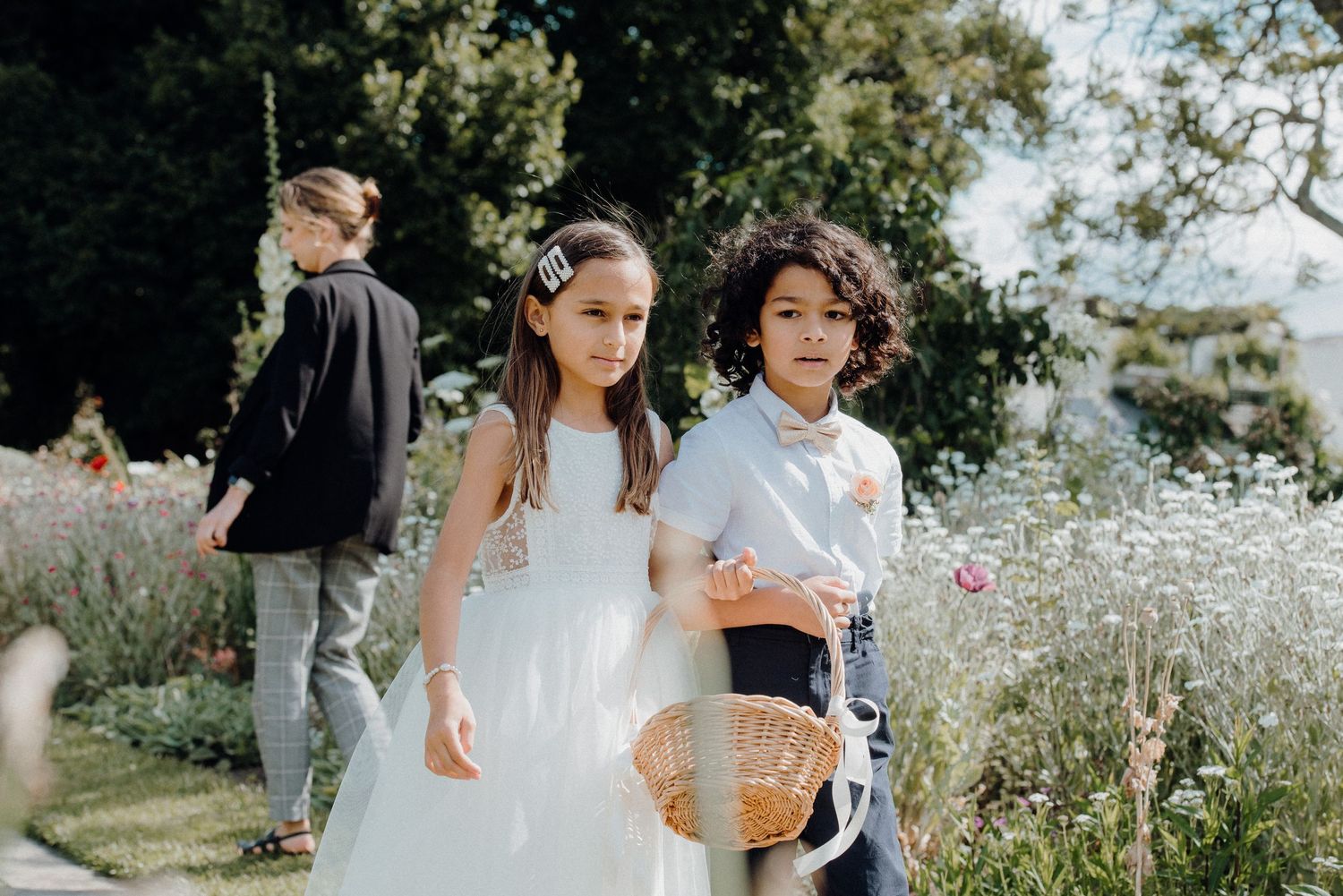Young attendants in formal wear walk through flowering meadow.