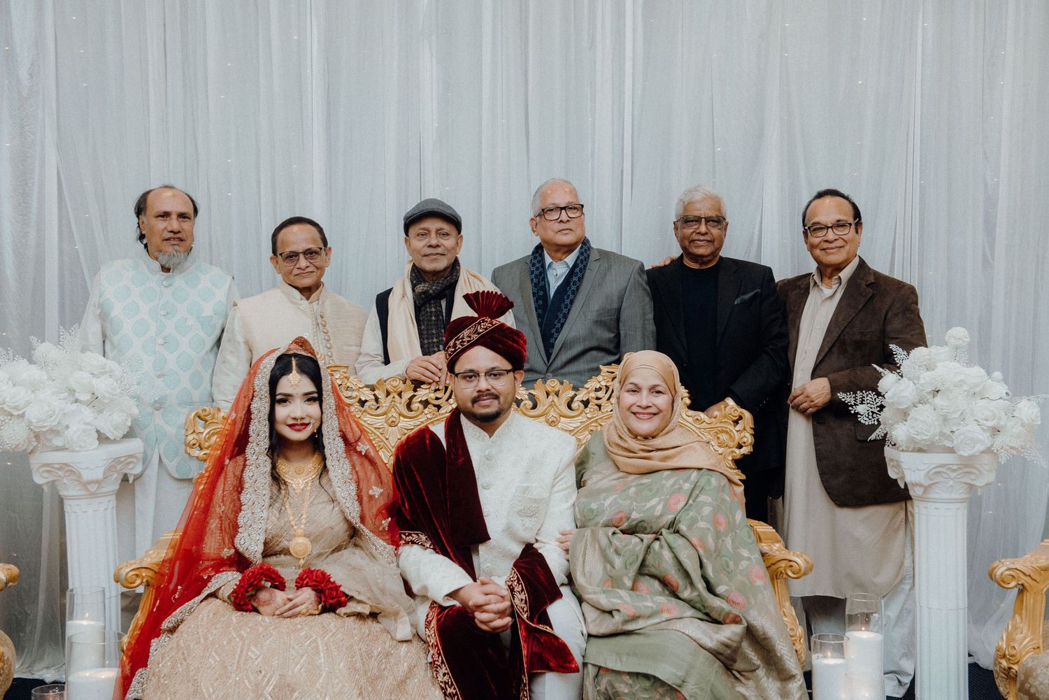Extended family portrait at South Asian wedding with traditional decor.