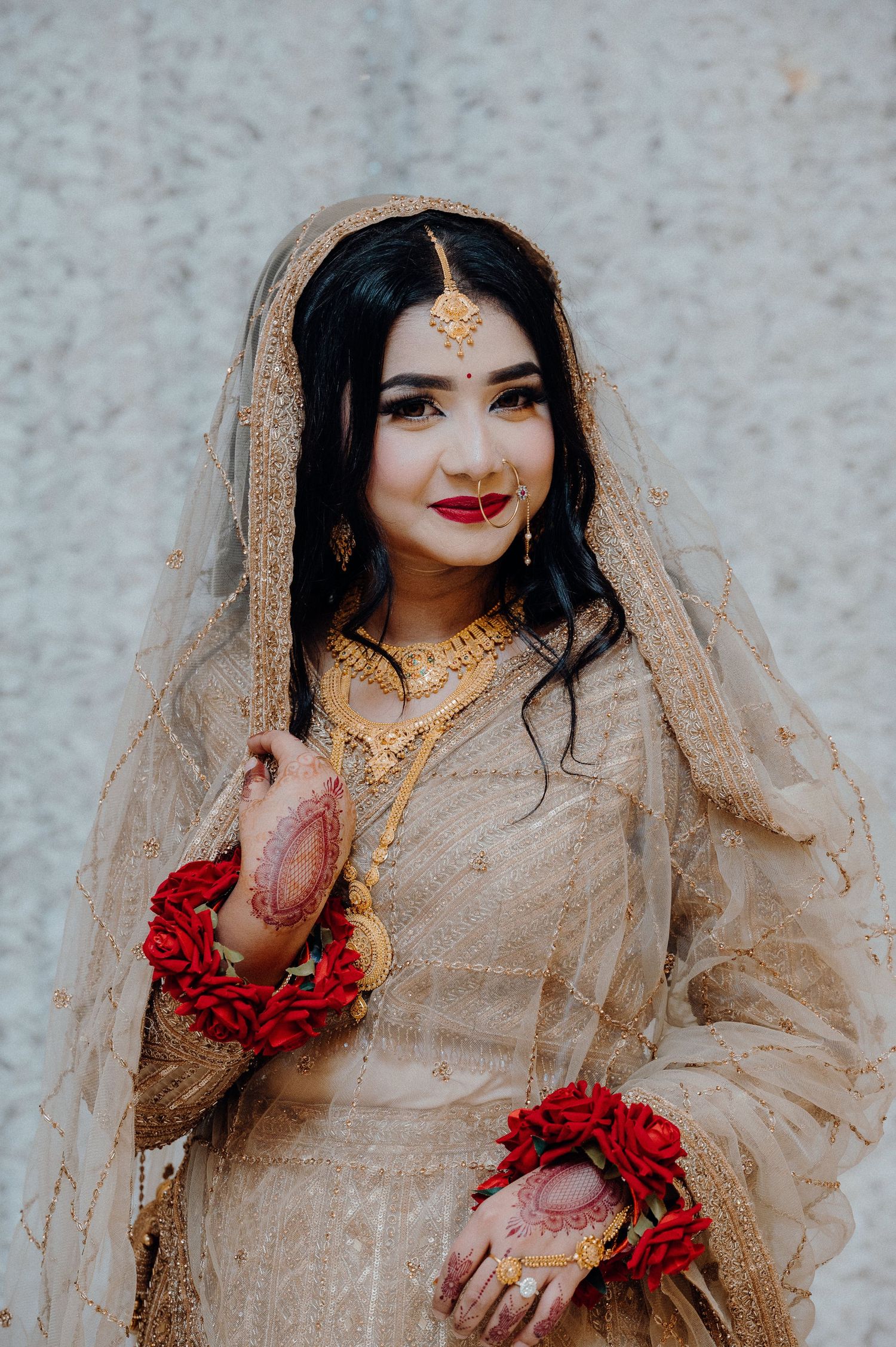 Bride in beige outfit with gold details poses wearing red floral jewelry on hands.