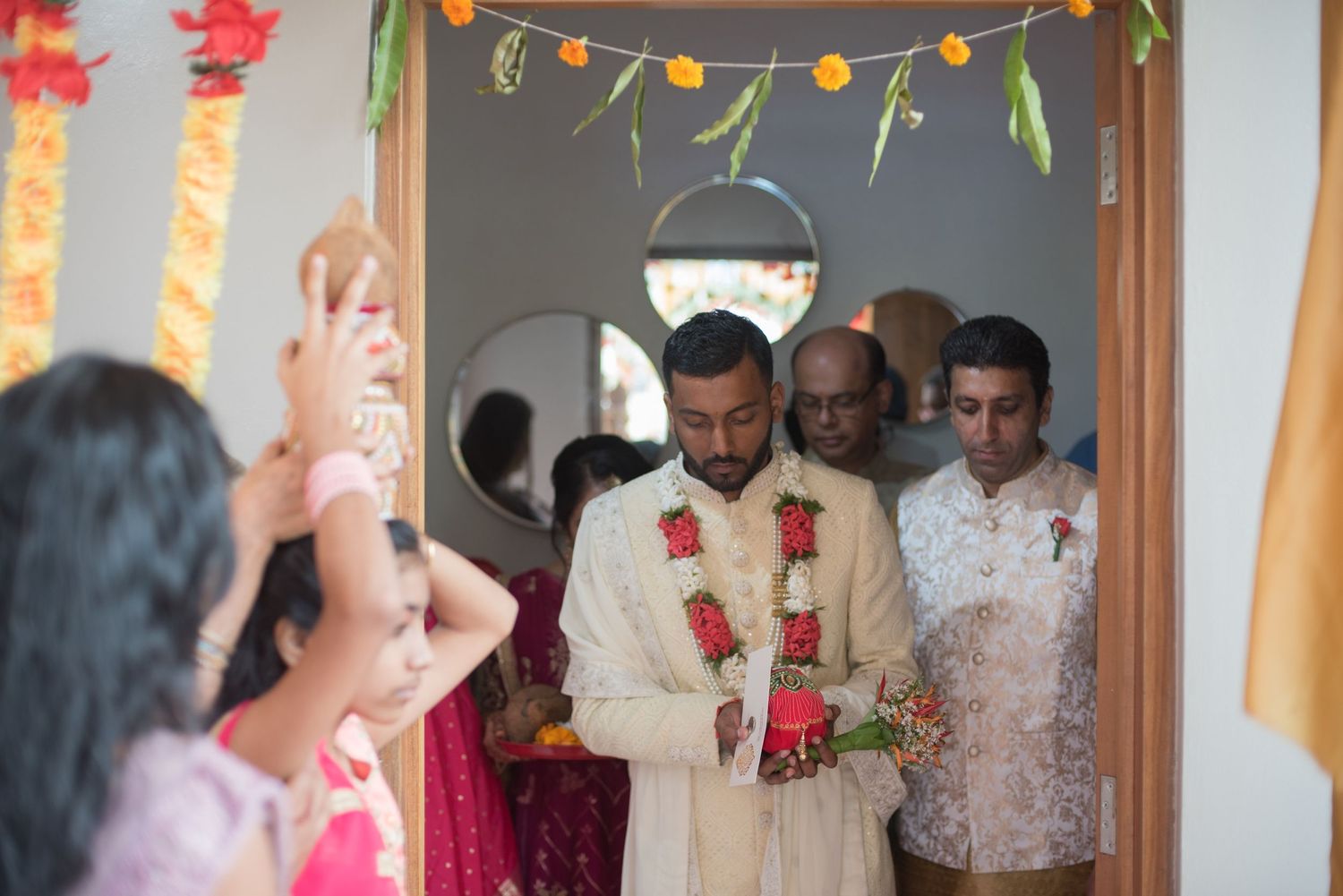 Wedding ceremony participants gather under decorative floral and light arrangements.