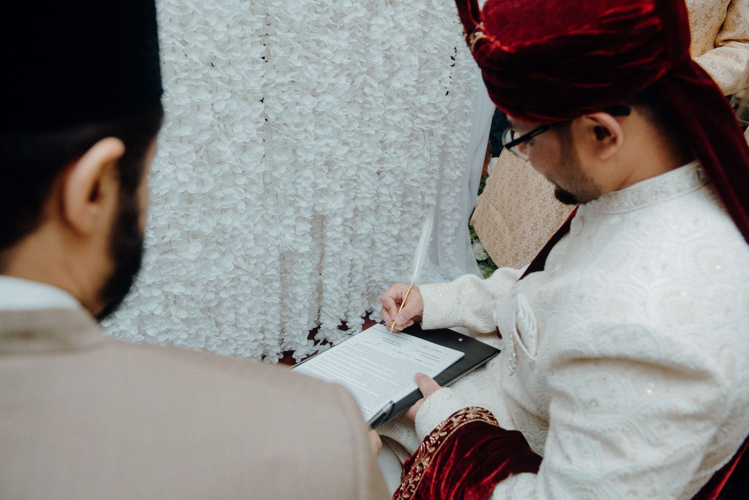 A couple signs documents during their wedding ceremony while wearing traditional attire.