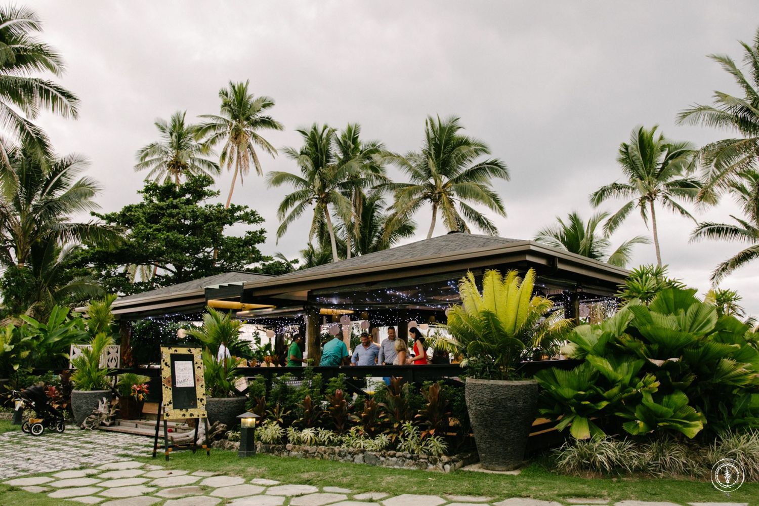 Tropical outdoor bar venue with palm trees and stone pathways.