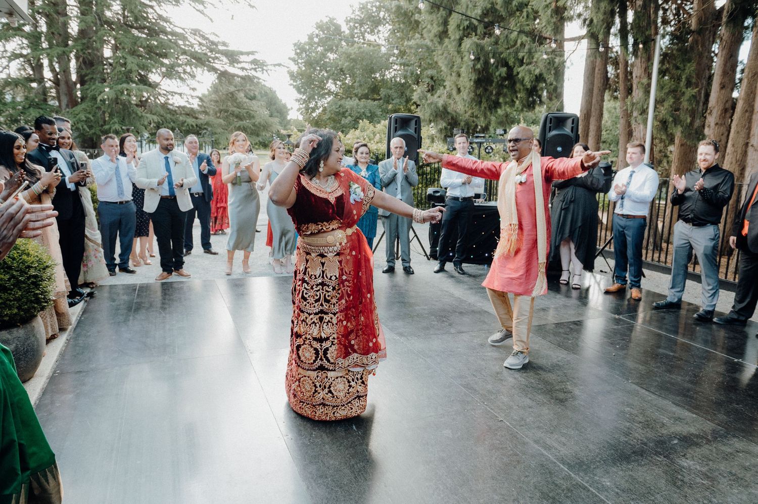 Wedding guests form circle around dancers on outdoor patio during celebration.