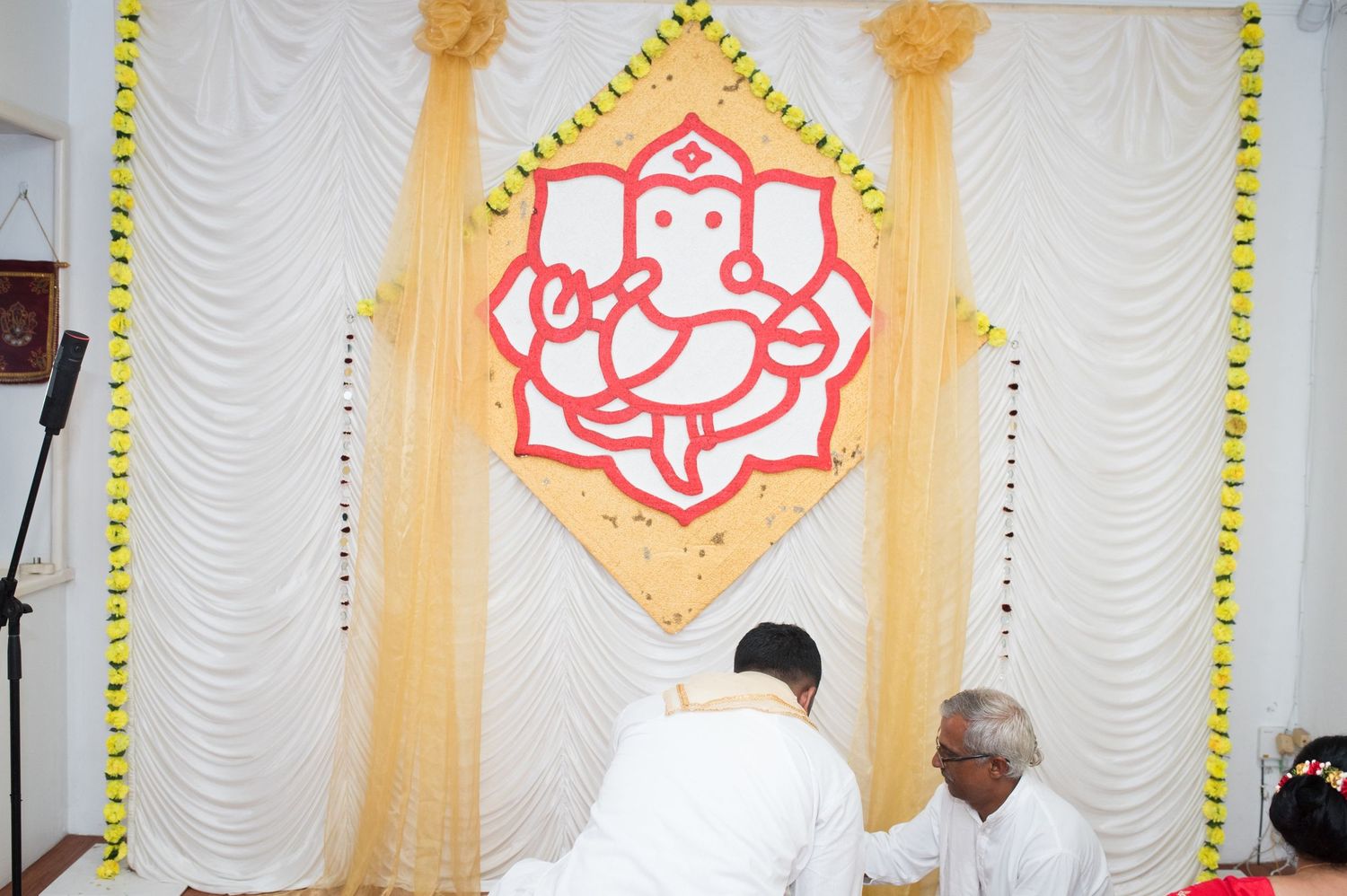 Red Ganesh symbol decorates white backdrop with yellow accents for wedding ceremony.
