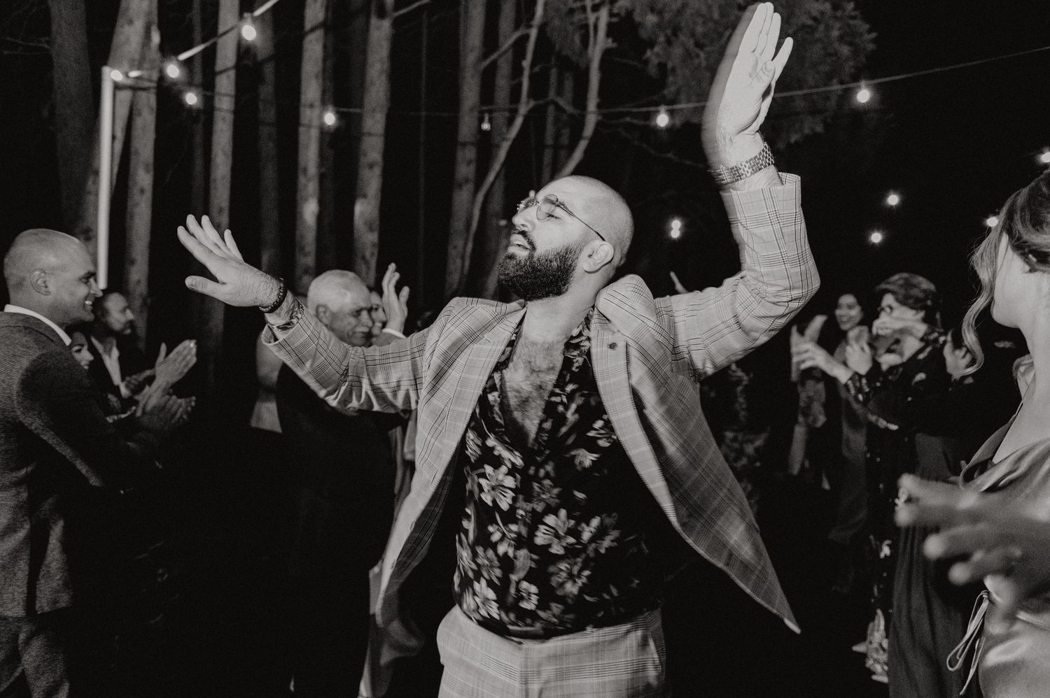 Person in formal attire dances joyfully with raised arms during an evening celebration.
