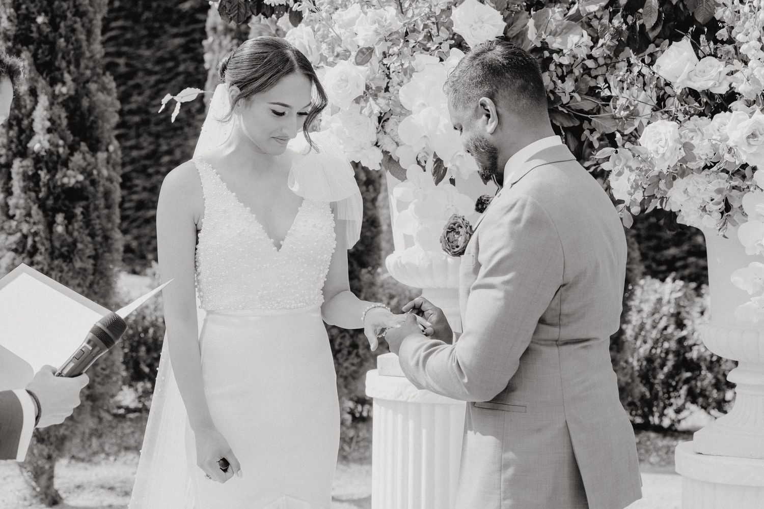 Black and white capture of an intimate wedding ceremony moment under floral decorations.