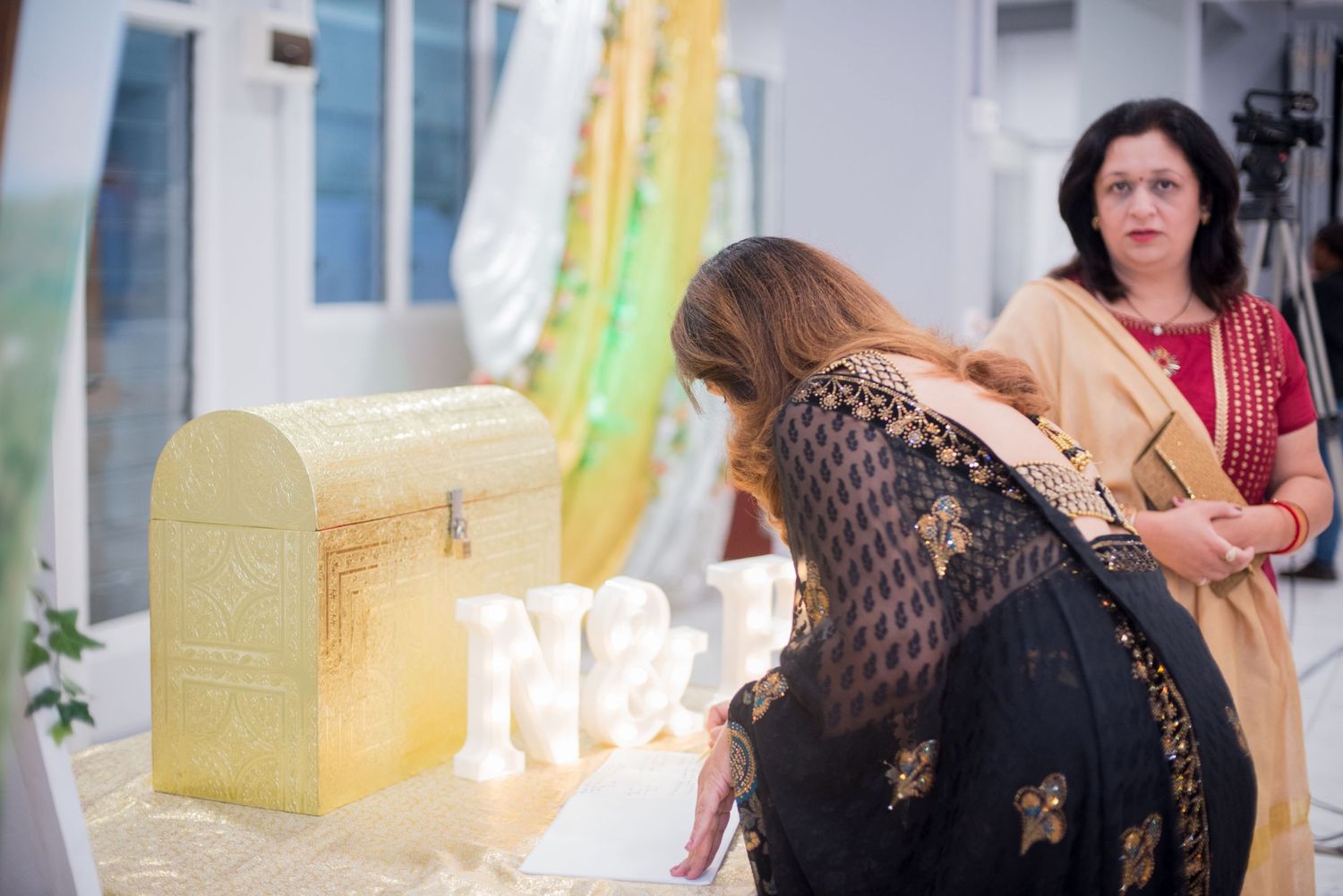 Decorative gold wedding card box with sheer drapes in background.