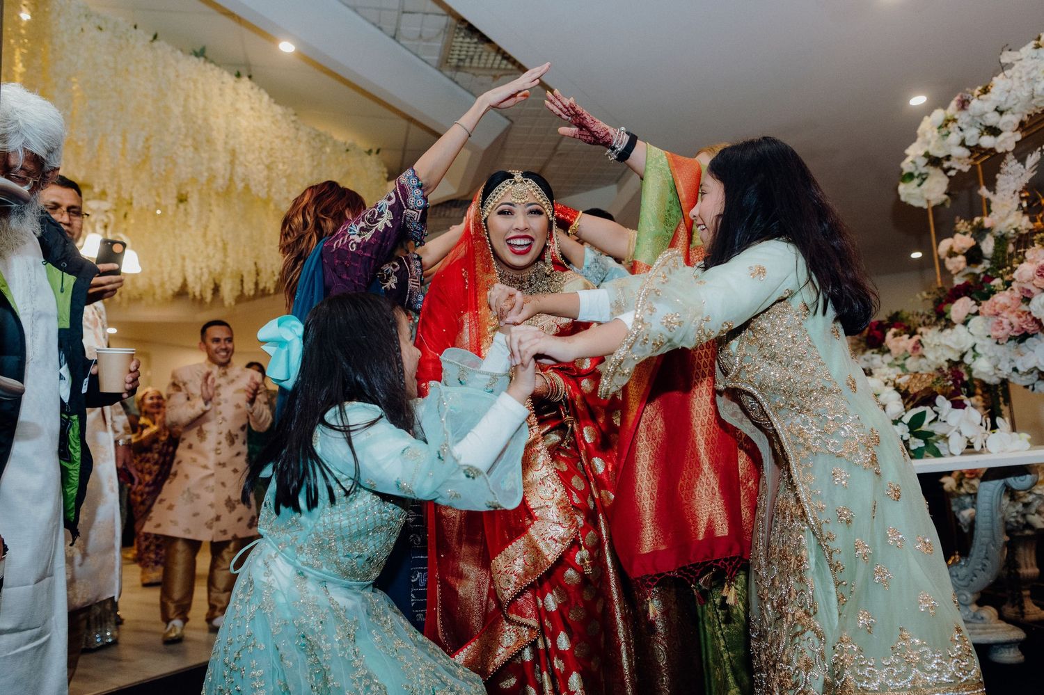 Energetic wedding celebration with guests dancing and jumping in colorful traditional outfits.