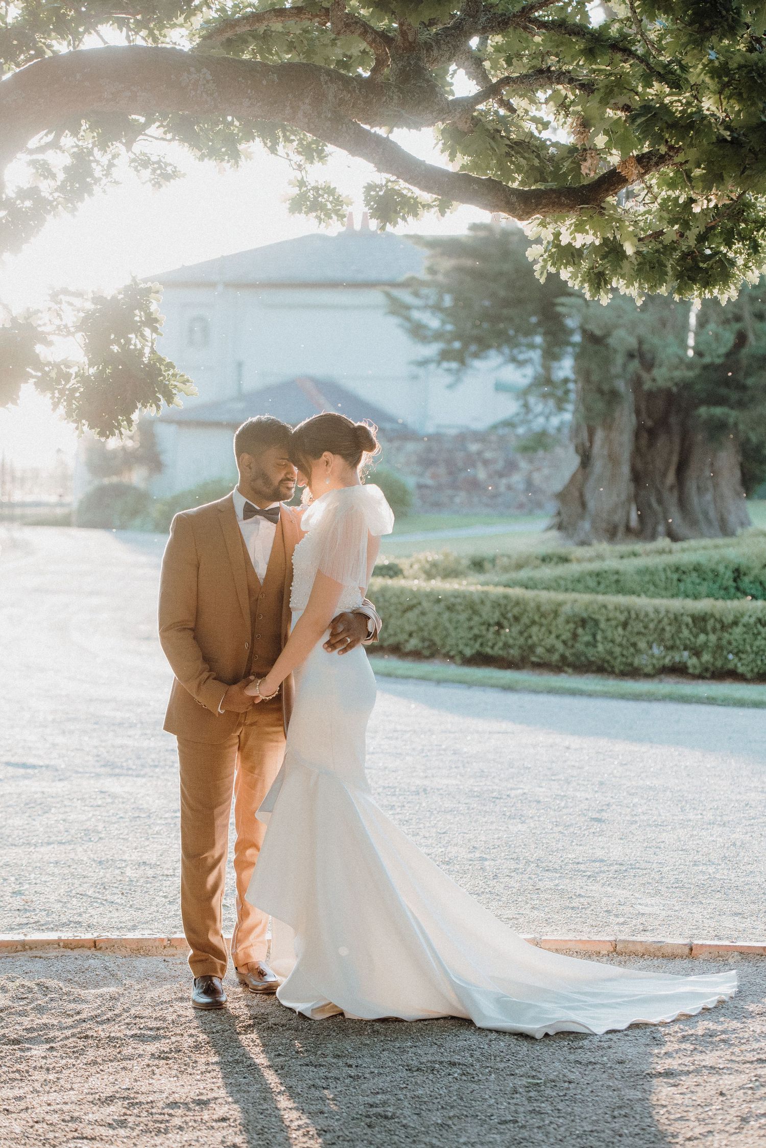 Newlywed couple shares an intimate moment under a tree branch during sunset.