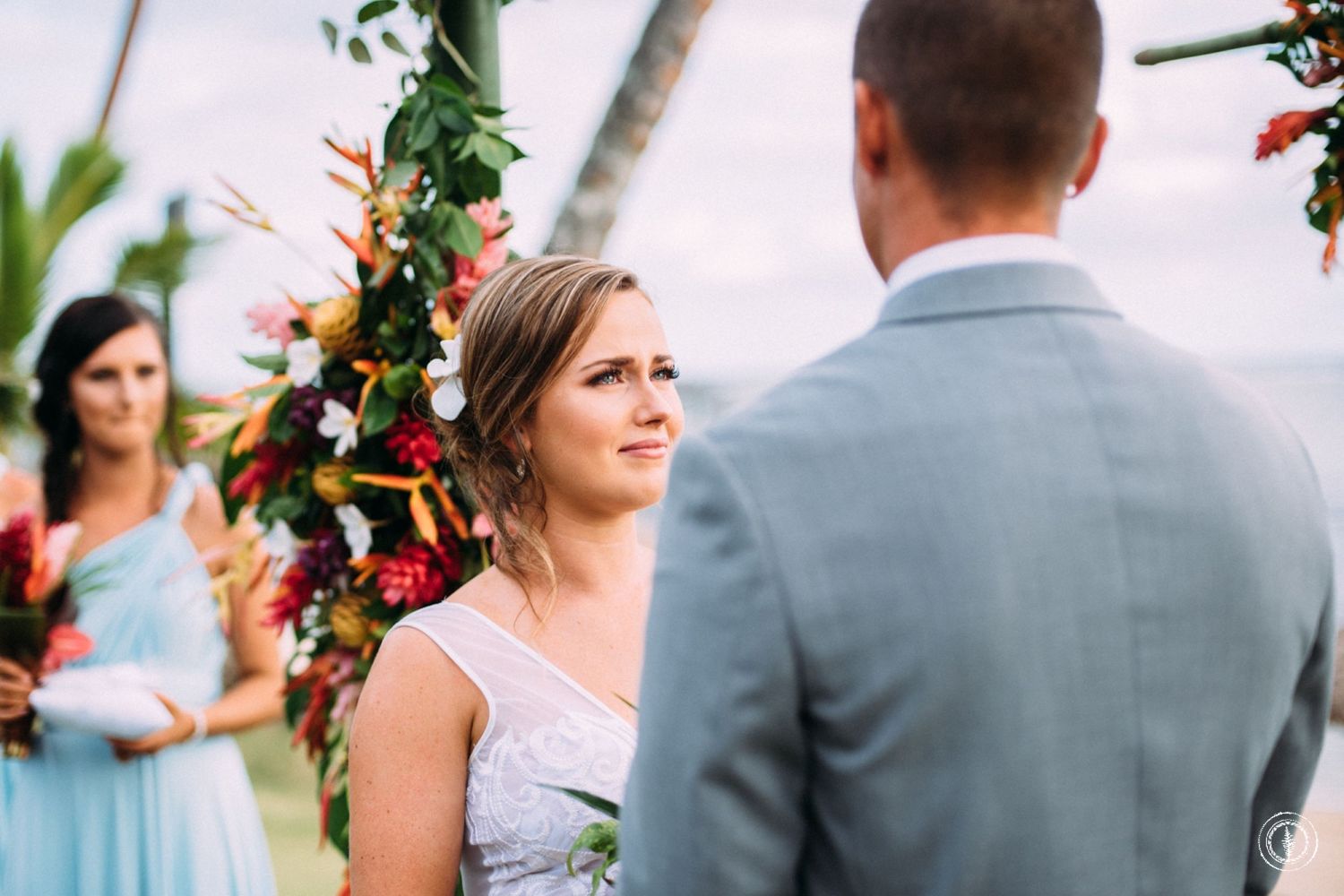 A close-up moment during a wedding ceremony with tropical floral decorations in the background.