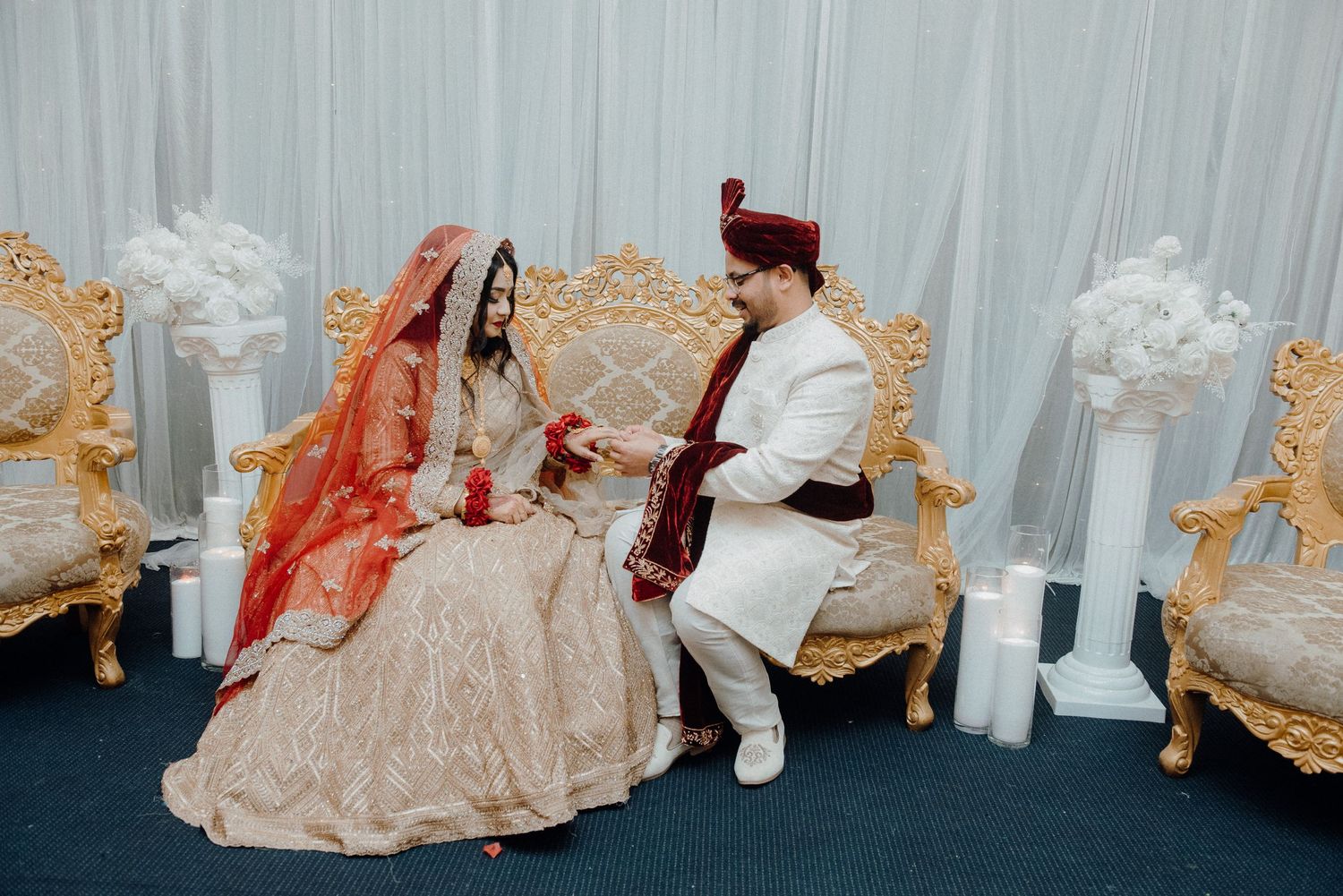 Traditional South Asian wedding couple seated on gold ornate chairs during ceremony.