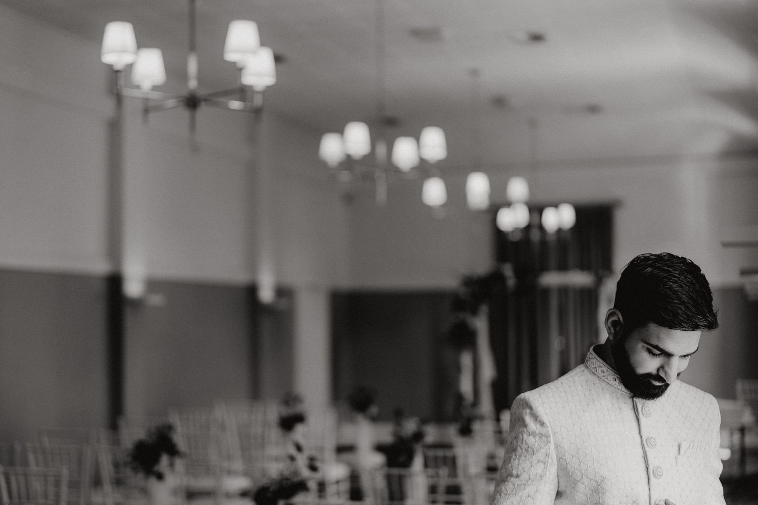 A moody black and white photograph of a wedding ceremony space with elegant chandeliers and white seating.