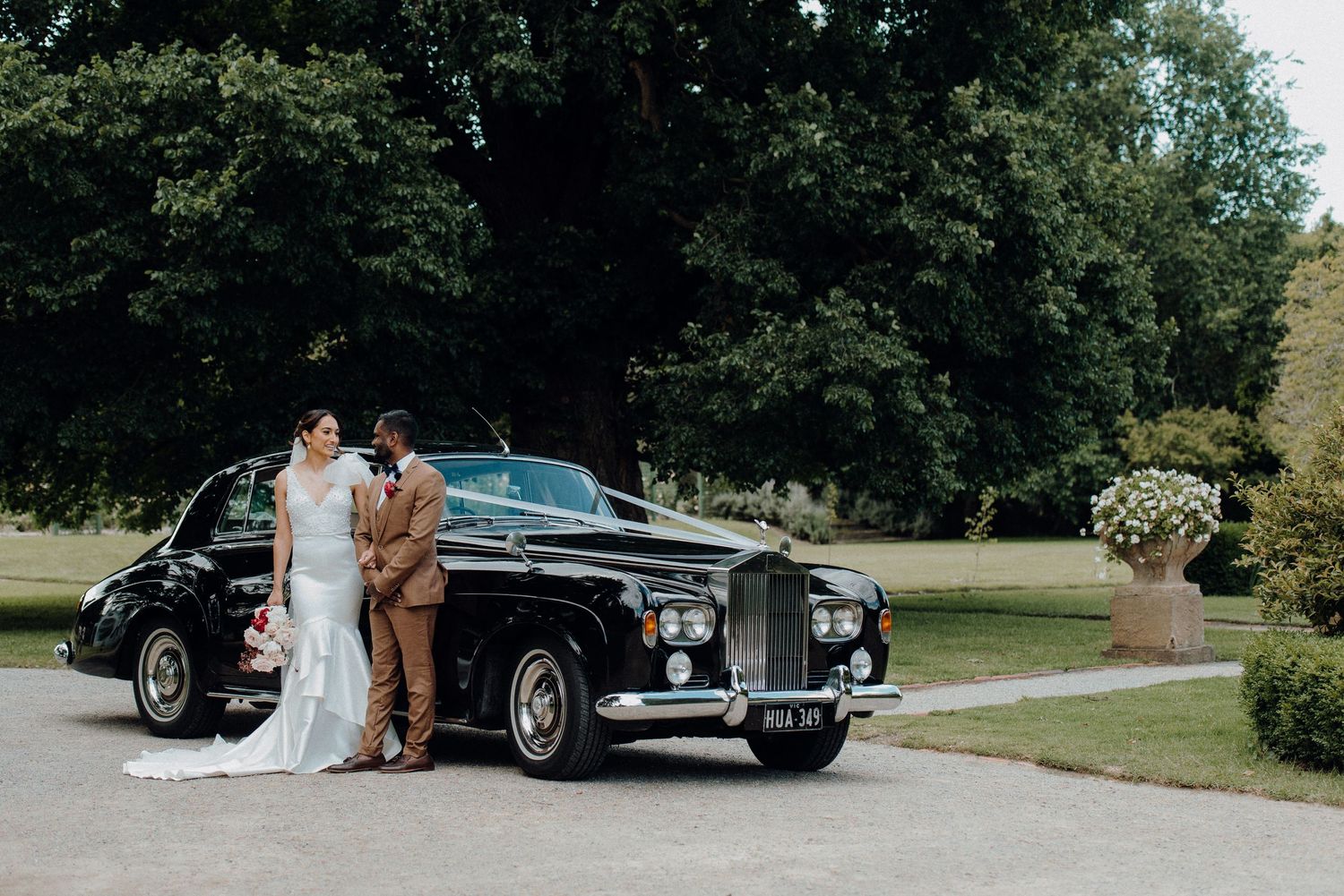 Couple poses with classic vintage Rolls Royce at outdoor wedding venue.