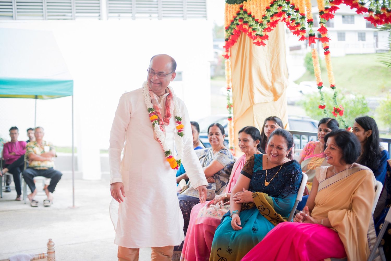 Person in white kurta with flower garland at Indian wedding celebration.