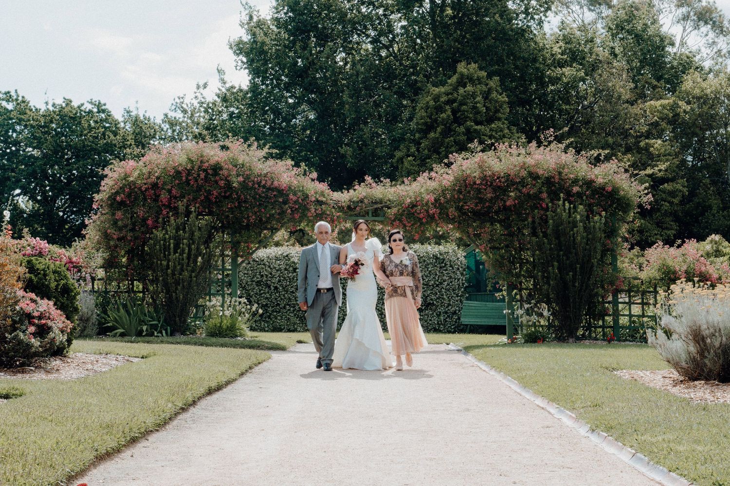 An outdoor wedding ceremony under a beautiful floral arch surrounded by manicured gardens.