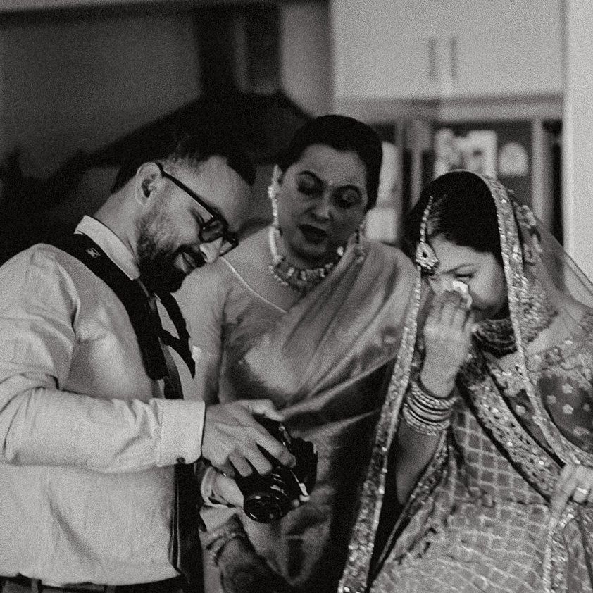 Black and white photo of a bride in bridal attire crying while a photographer shows her images on his camera.