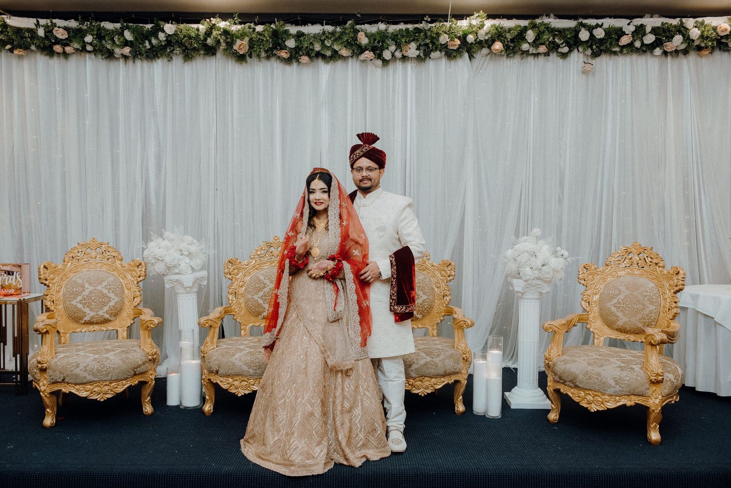 Elegant wedding portrait with gold chairs and floral archway decoration.