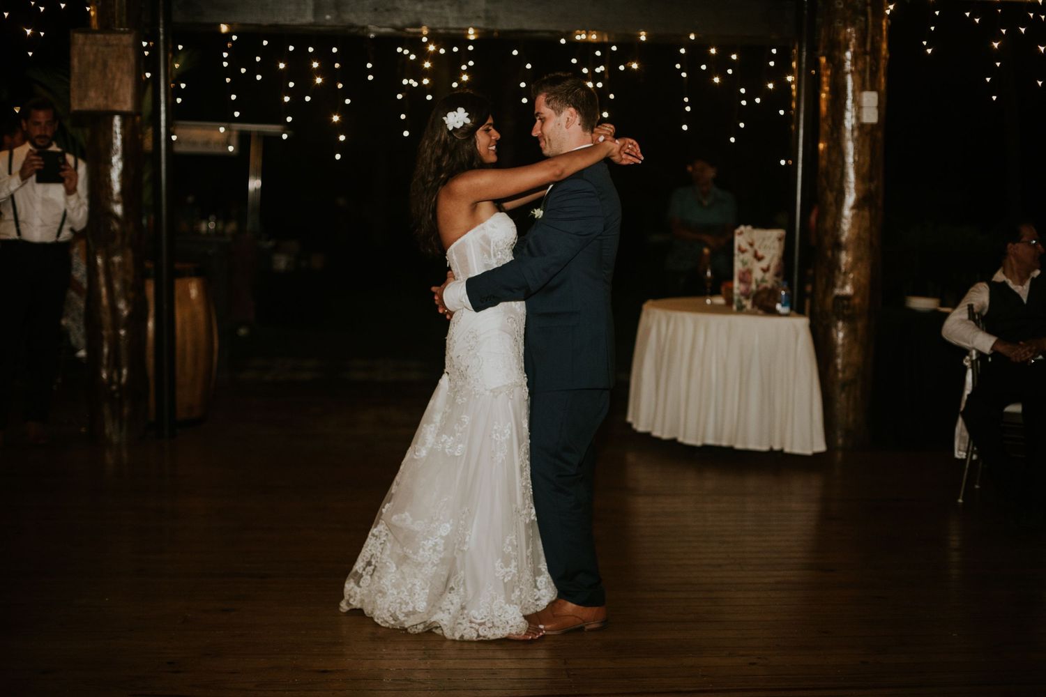 A romantic slow dance moment at a wedding reception under twinkling lights.