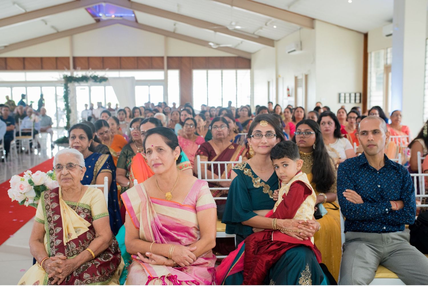 Large gathering of guests in colorful traditional attire seated at an indoor celebration.