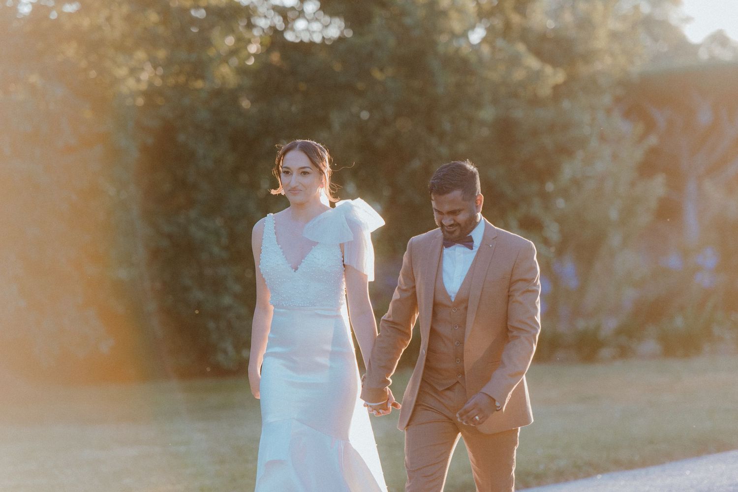 Couple strolling through a sunlit garden in wedding attire.