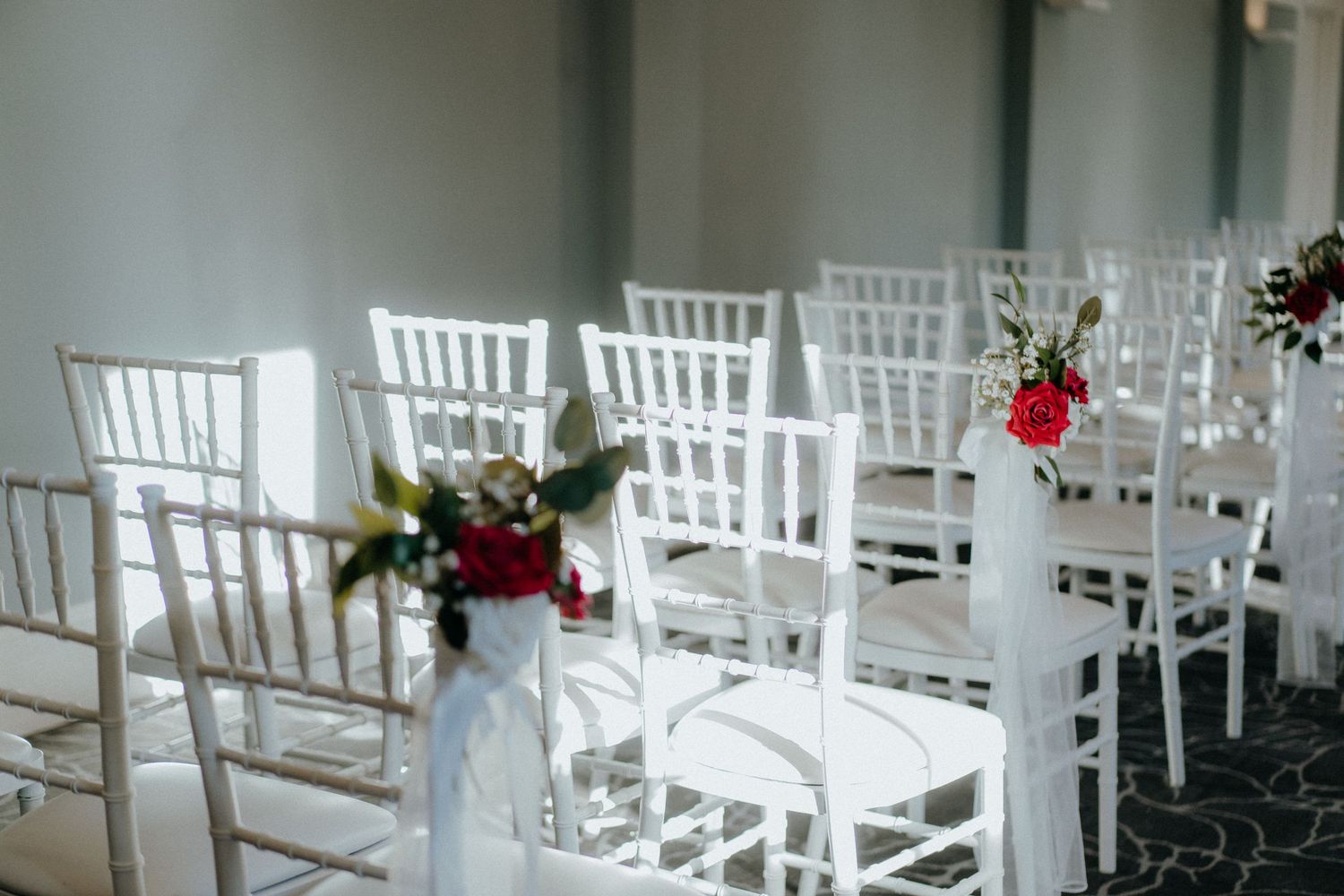 Elegant white Chiavari chairs decorated with red and white floral arrangements for a wedding ceremony.