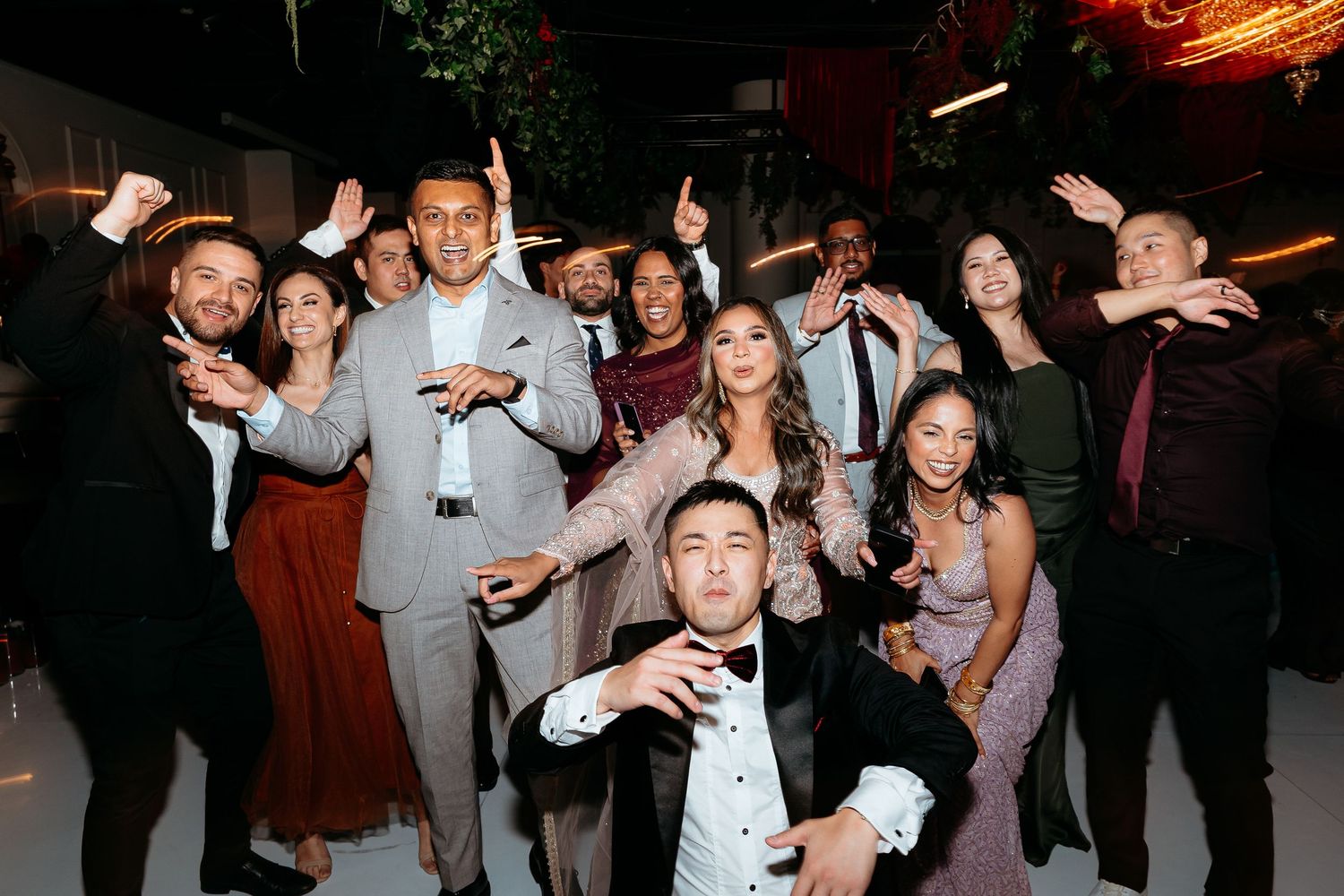 Joyful wedding guests dance and celebrate together at a lively indoor wedding reception party.