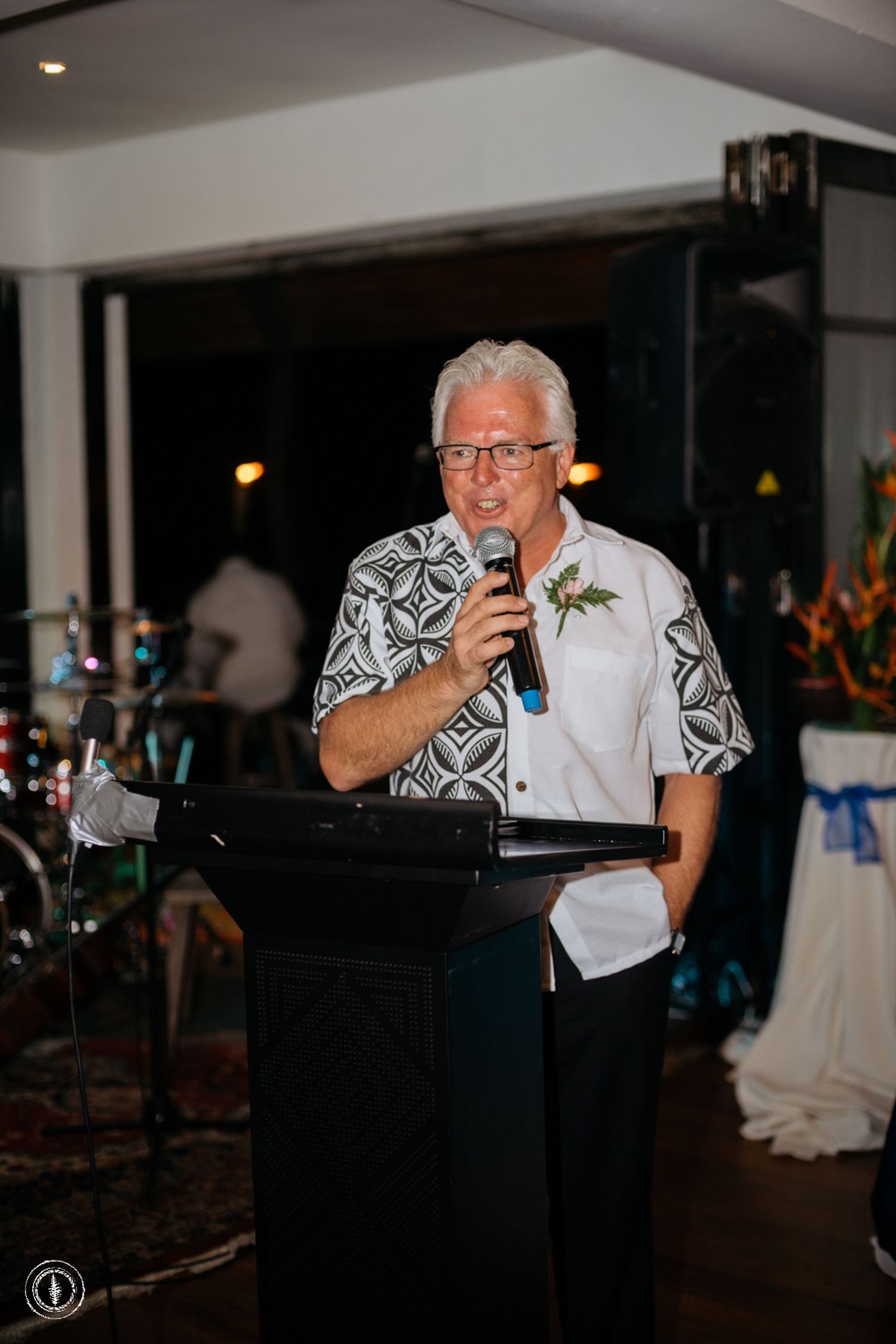 A speaker in a patterned shirt delivers remarks from a podium during an evening event.