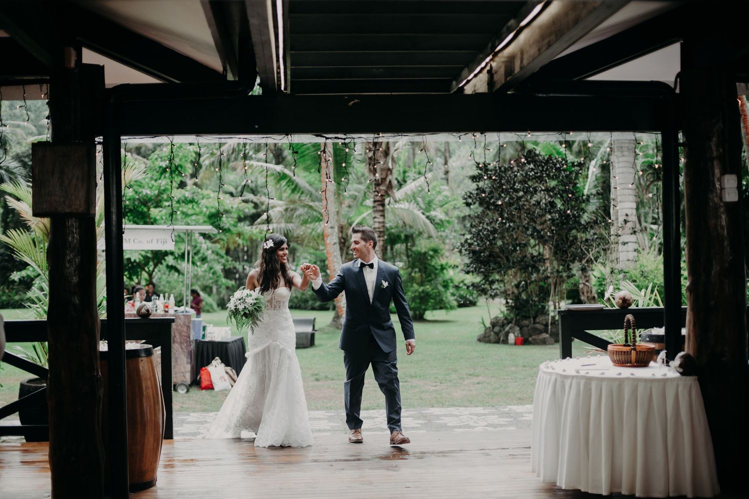 Covered outdoor wedding reception area with white tables and tropical garden backdrop.