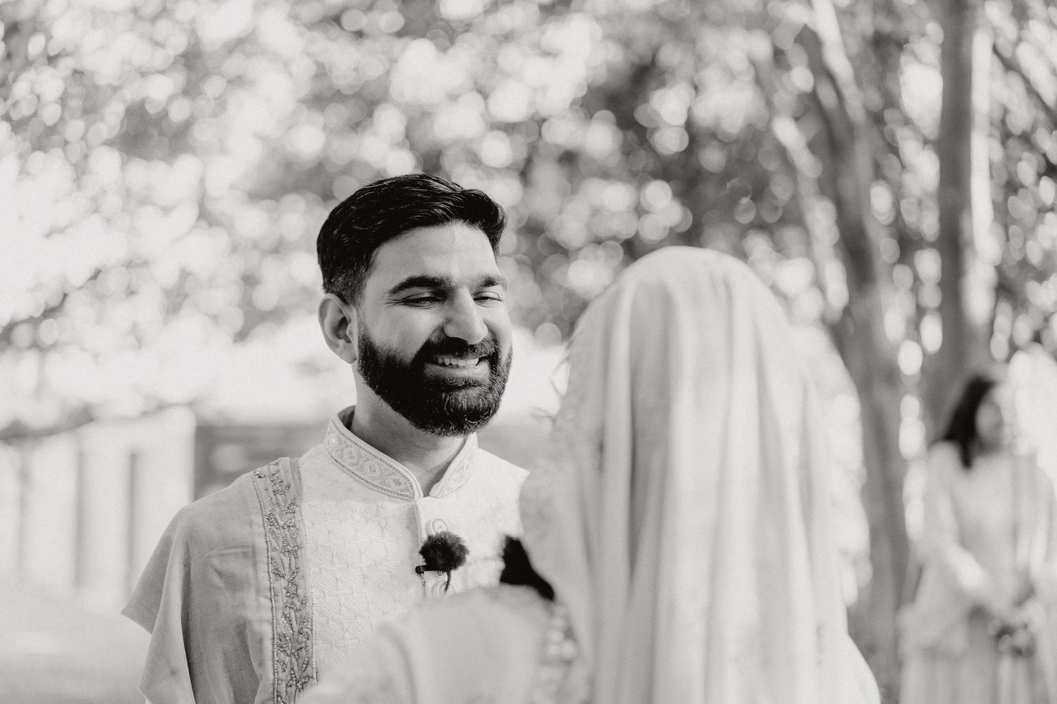 Black and white portrait capturing a candid moment during an outdoor wedding ceremony.