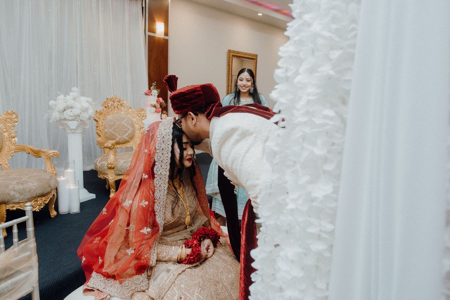 A traditional wedding ceremony moment captured with ornate decorations and white curtains in the background.