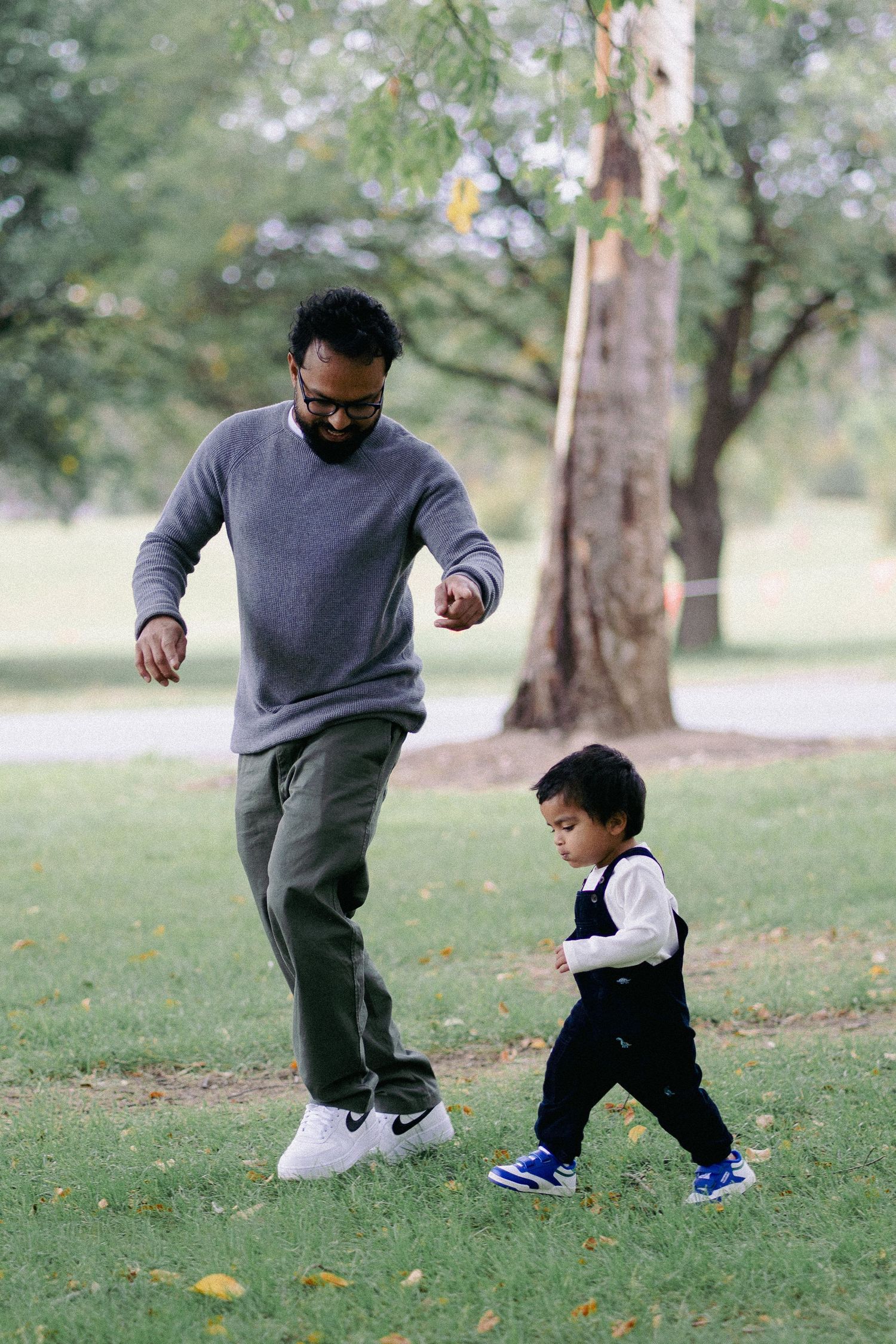 Father and toddler son playing together on green grass in a park setting.