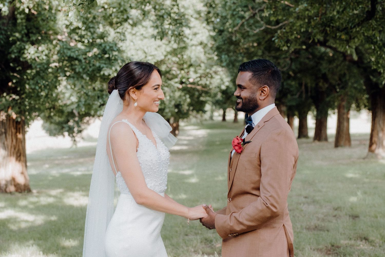 A joyful wedding couple holds hands outdoors surrounded by trees on their special day.