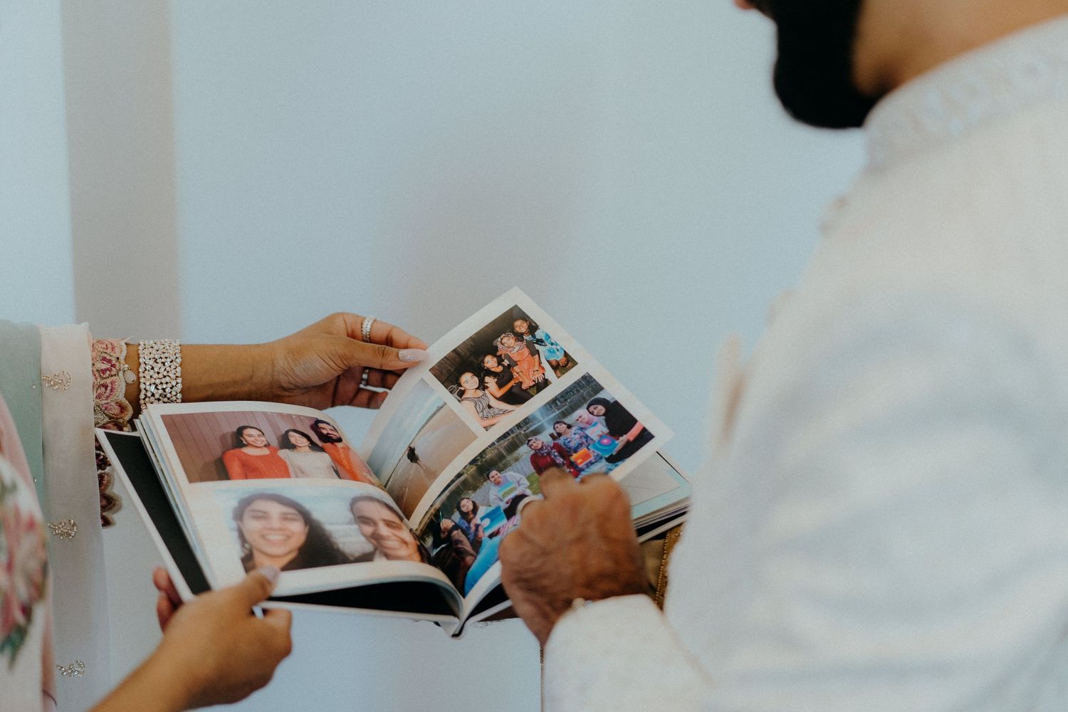 Hands holding and looking through a wedding photo album with multiple photographs.