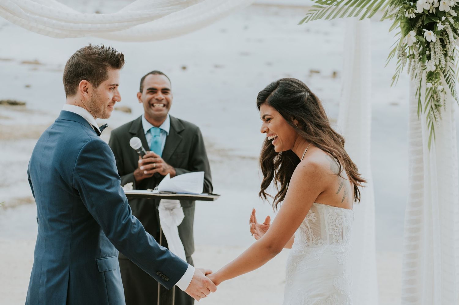 A joyful moment during beach wedding ceremony as couple exchanges vows under floral arch.