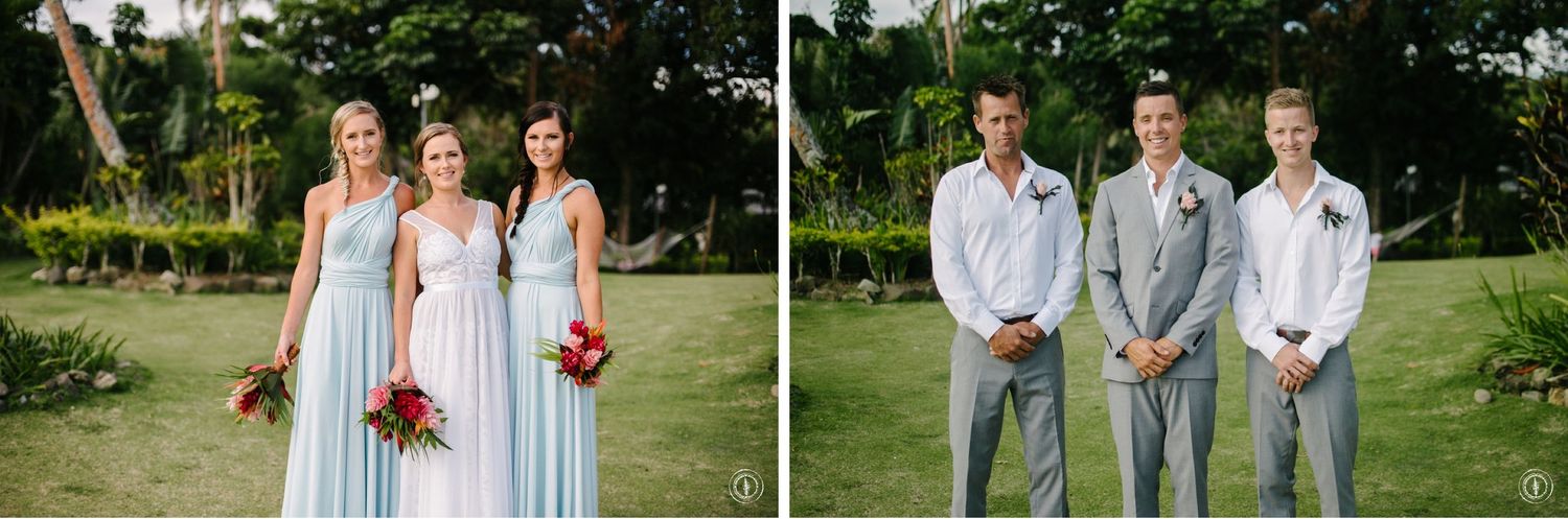 Wedding party members in coordinated pastel blue and white attire posing in garden setting.
