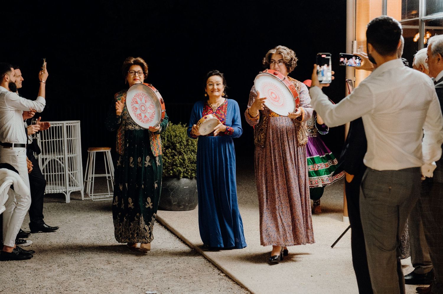 Wedding guests in traditional cultural attire dancing outdoors at night.