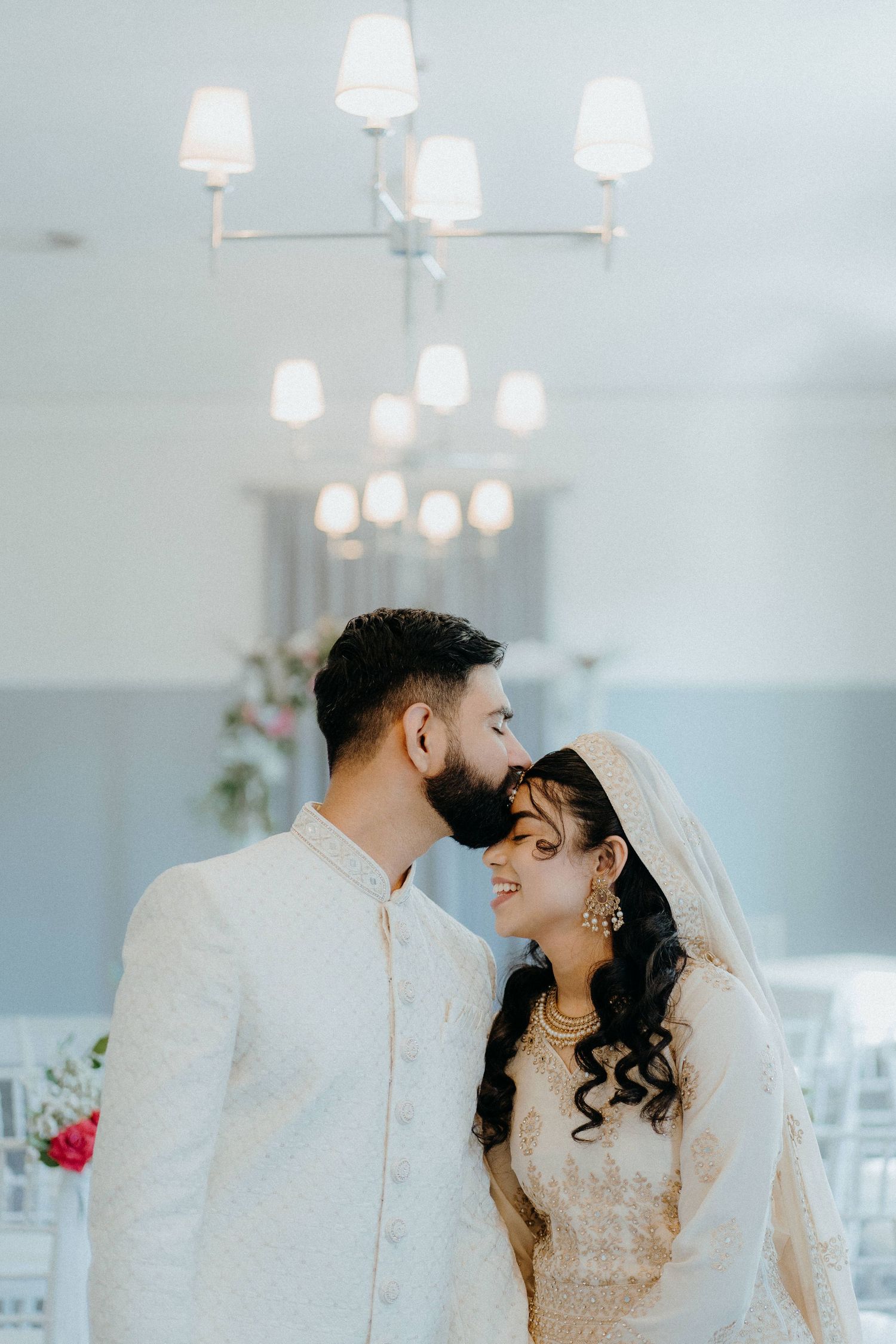 An intimate wedding portrait under elegant white chandeliers in a bright ceremony space.