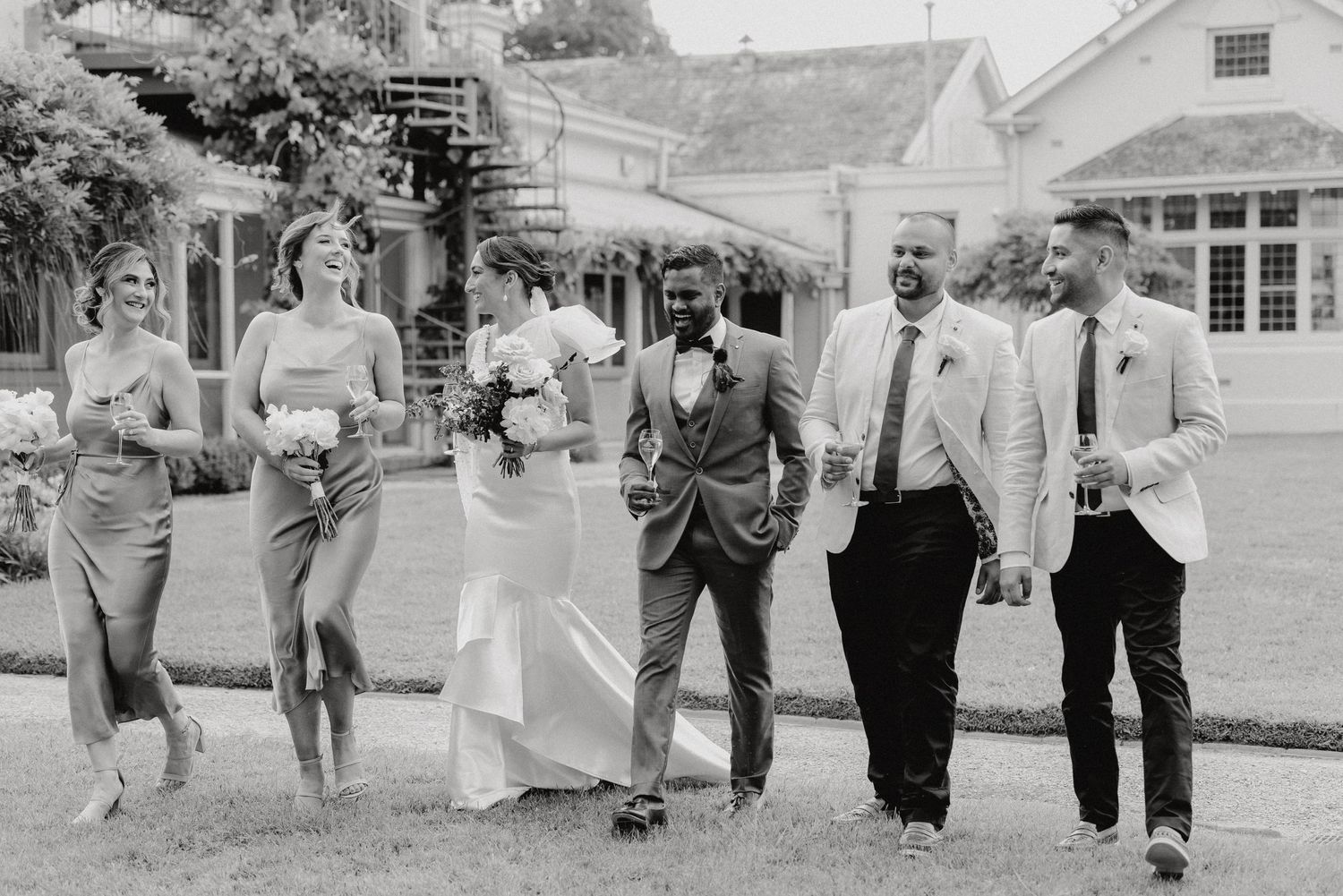 Black and white photo of wedding party walking together on grassy lawn.