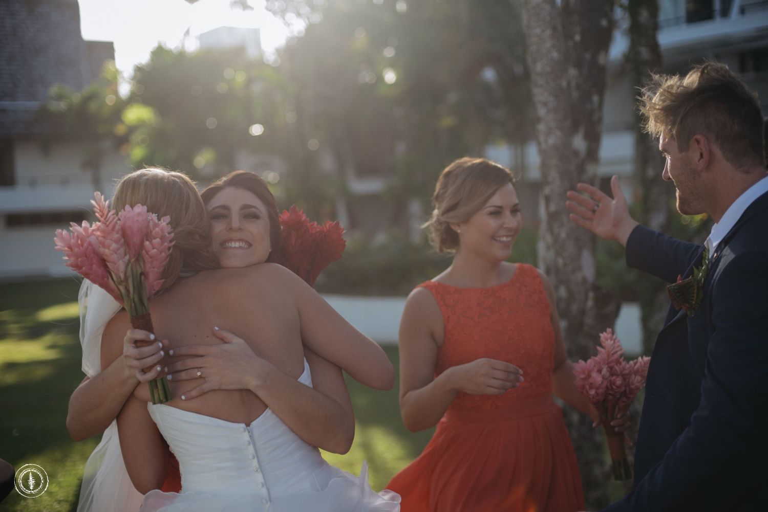 Wedding party celebrating outdoors with coral flowers and sunset lighting.