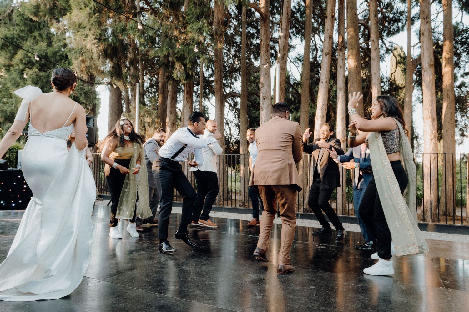Wedding guests dancing on an outdoor patio surrounded by tall eucalyptus trees.