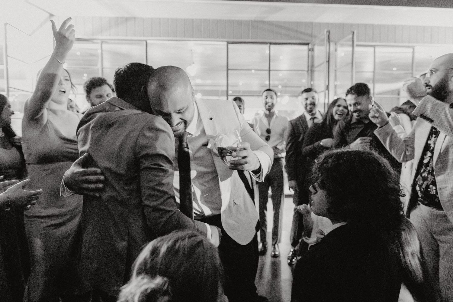 Black and white photo of guests dancing and celebrating at an indoor wedding reception.