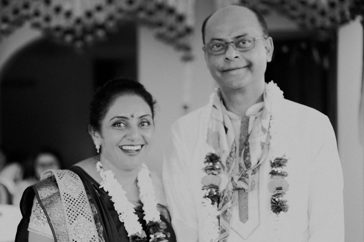 Couple in traditional Indian attire smiling at camera in black and white portrait.