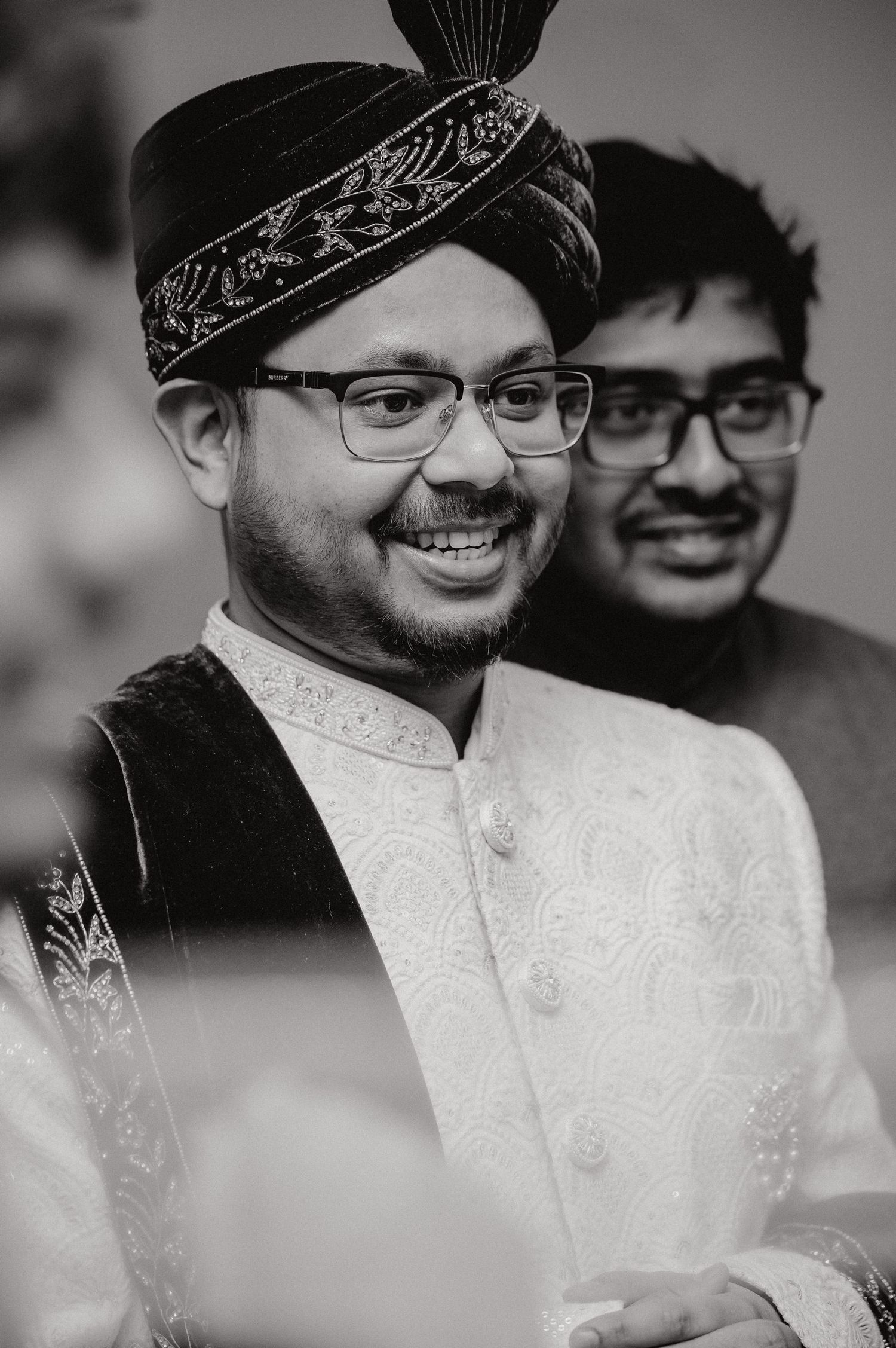 Traditional groom wearing embroidered sherwani and decorated turban in black and white.
