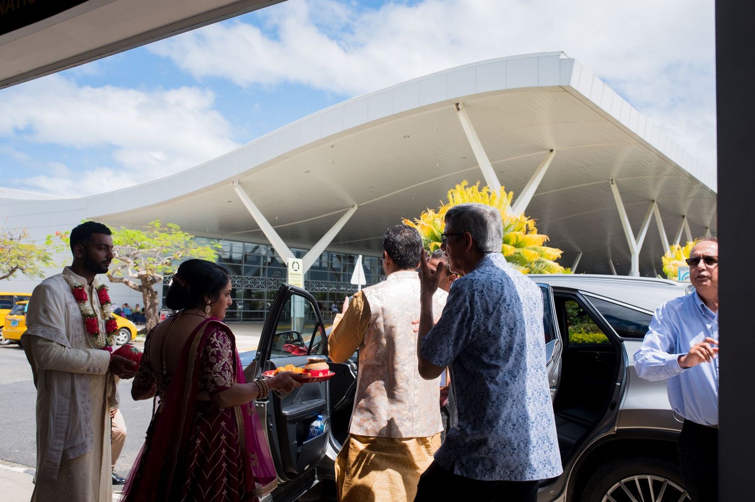 People in traditional Indian clothing gather outside a modern building with sunflowers.