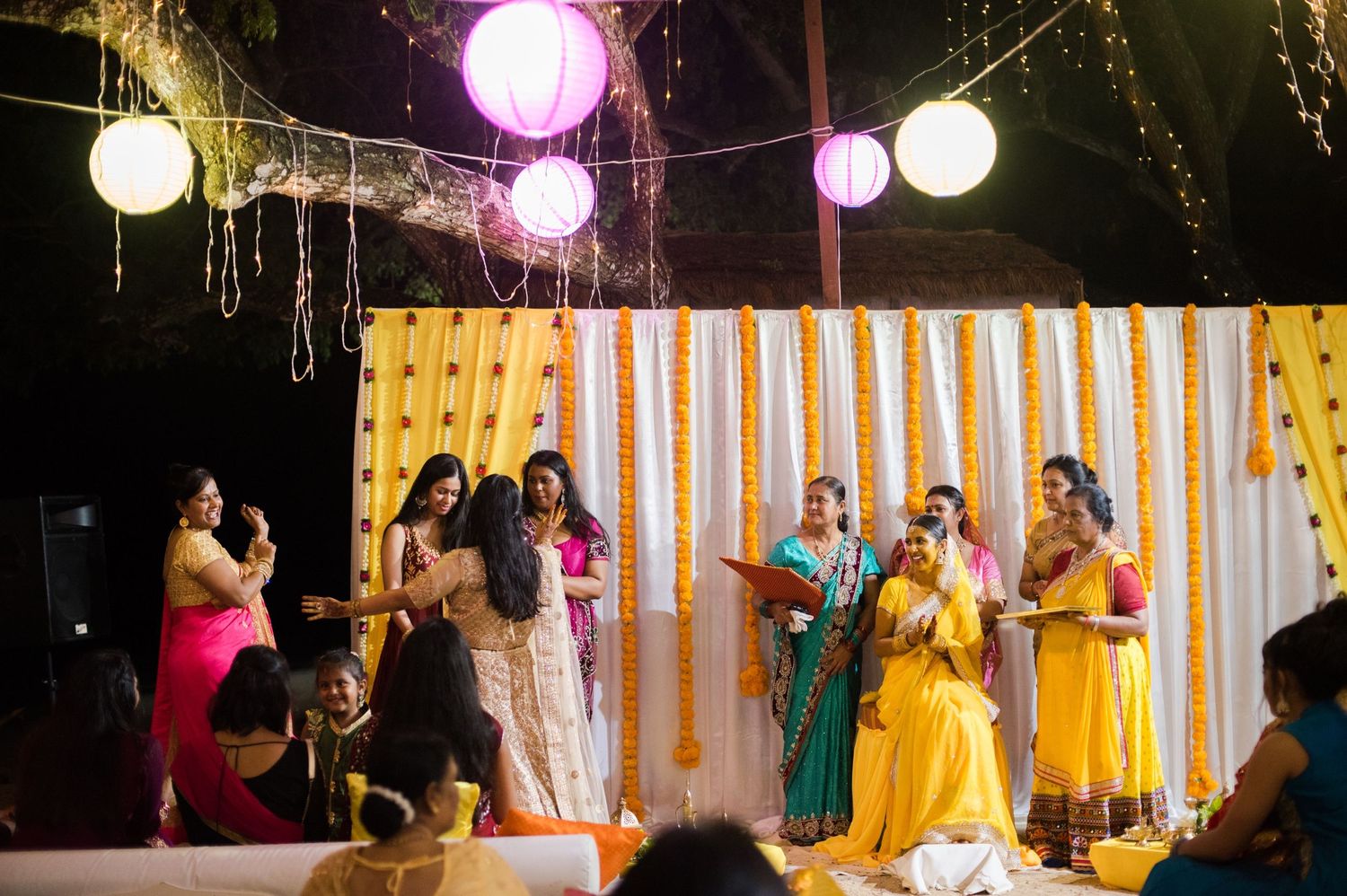Colorful Indian wedding celebration at night with hanging paper lanterns and decorative backdrop.