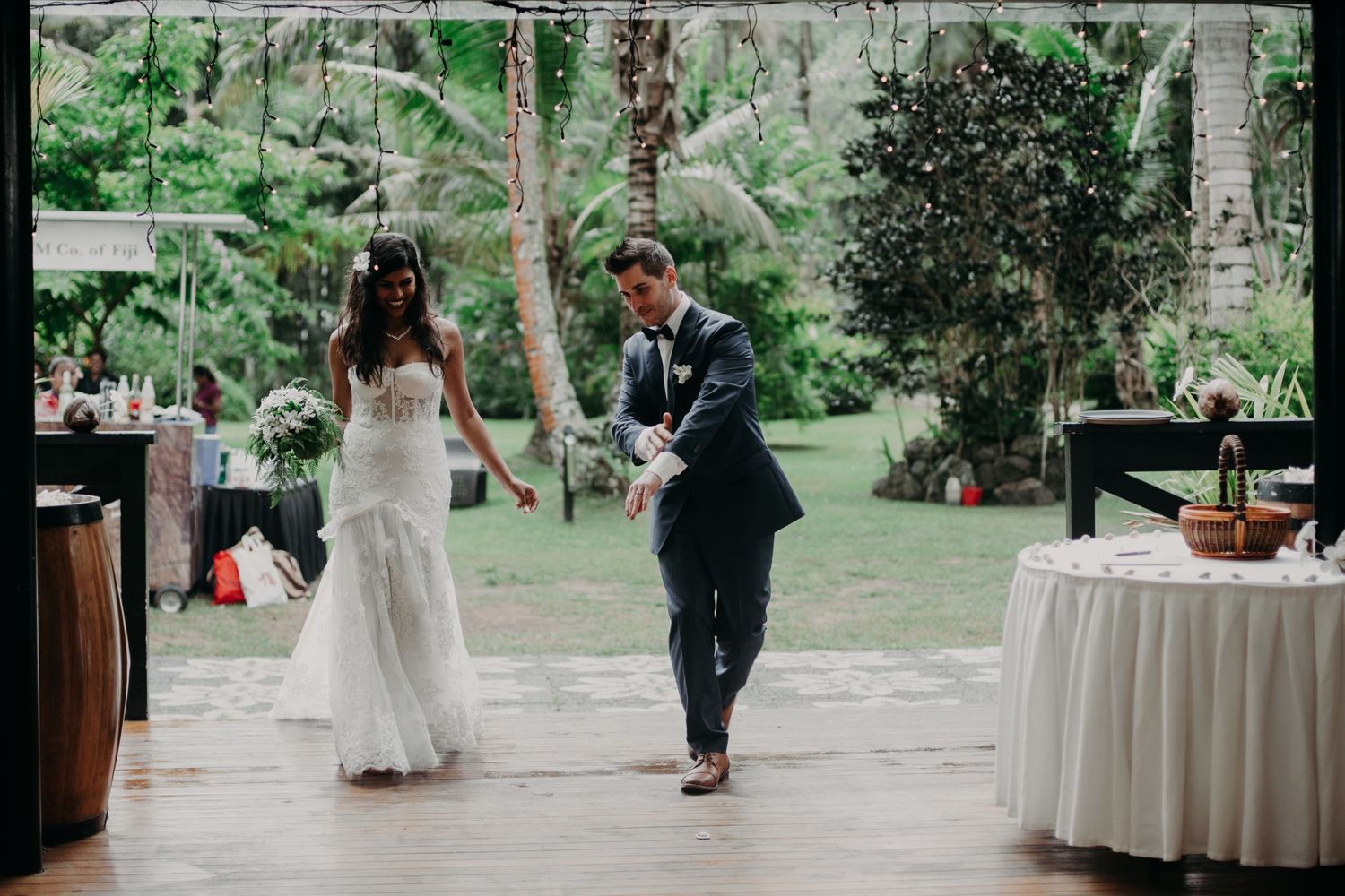 Reception venue with wooden beams and white tables set against a lush tropical garden backdrop.