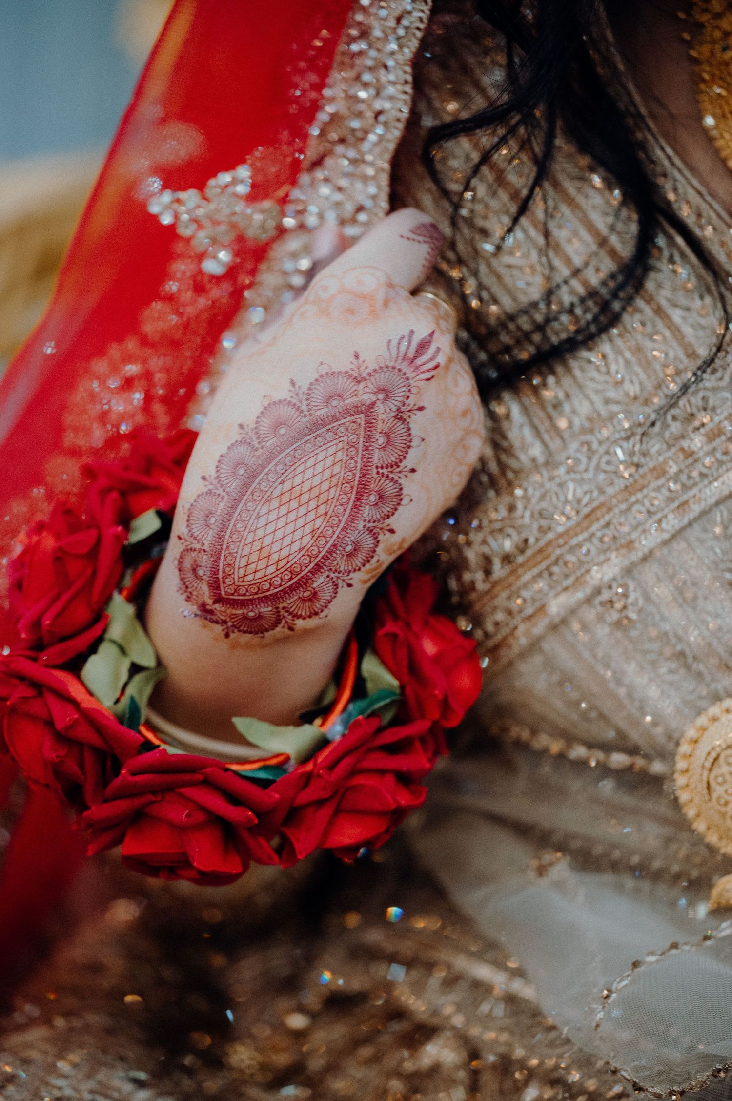 Close-up of intricate henna design on hand with red roses and sparkly fabric details.