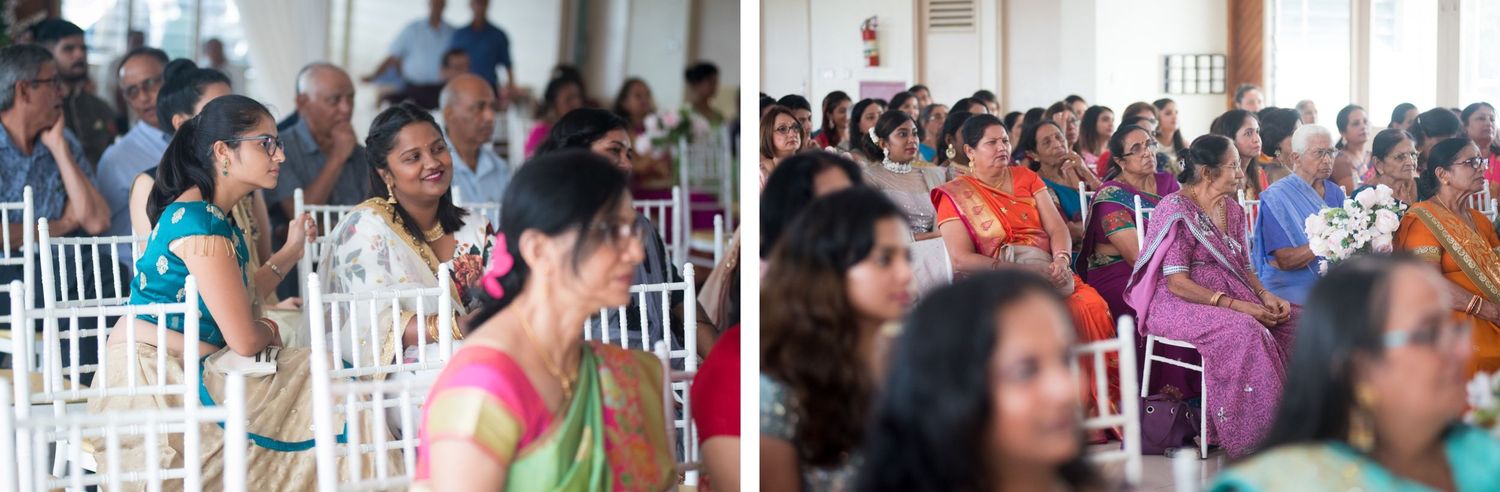 Guests seated in white chairs watch intently during an indoor wedding ceremony.