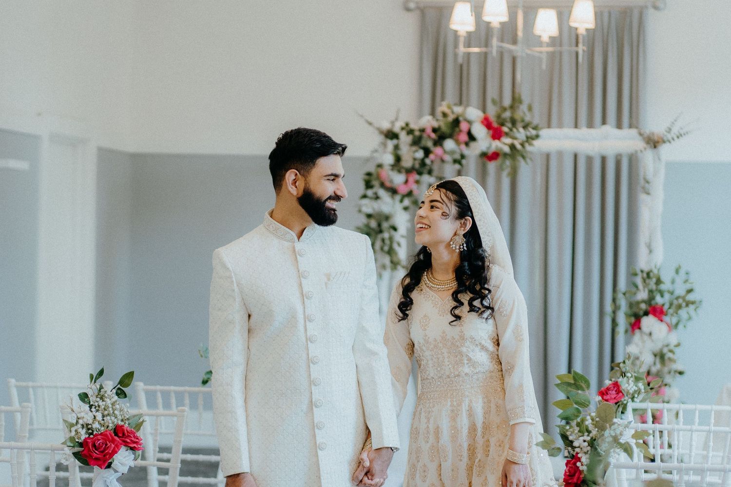 A bright wedding portrait in a modern venue with floral decorations and chandeliers.