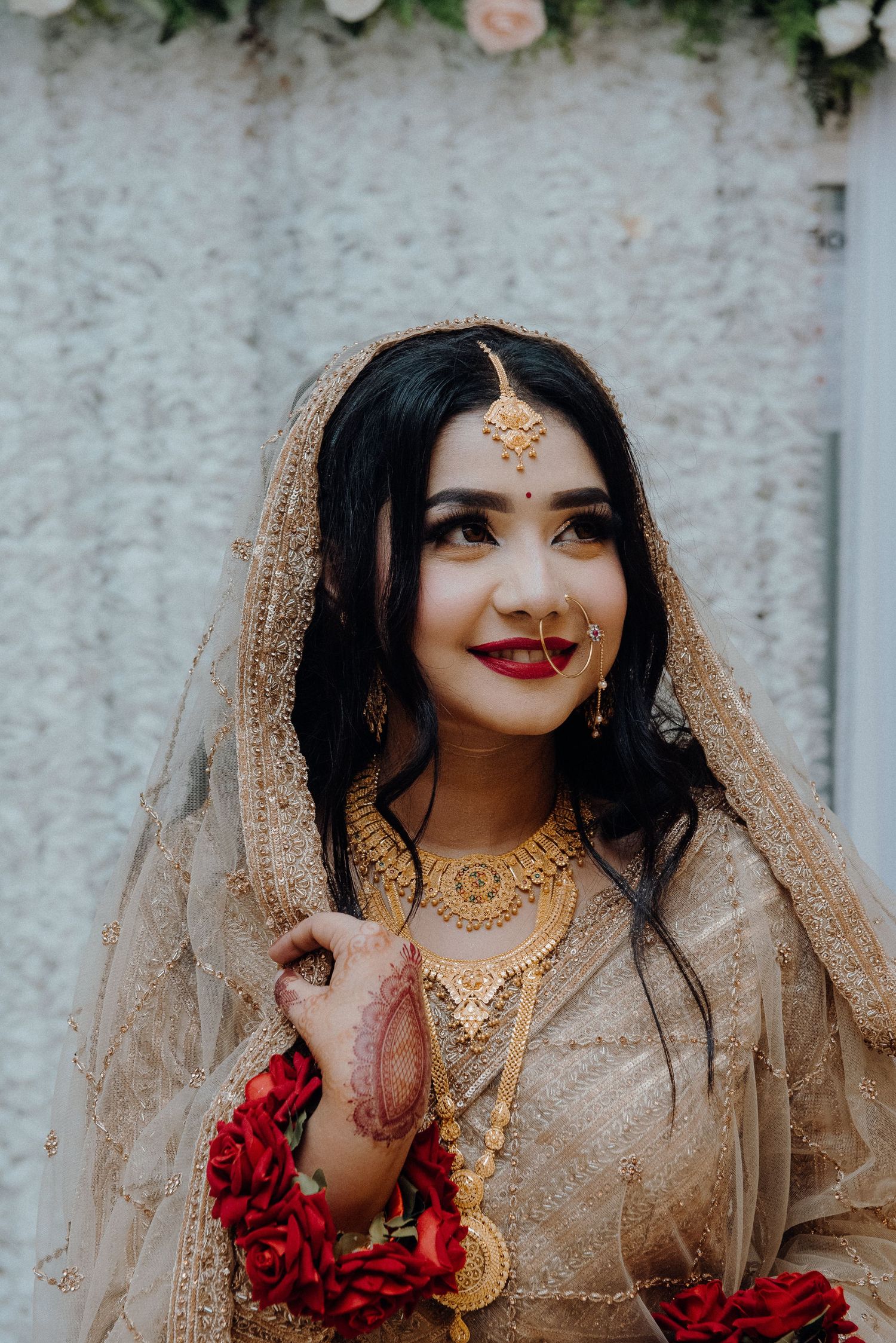 Traditional South Asian bridal portrait with gold jewelry and beige outfit.